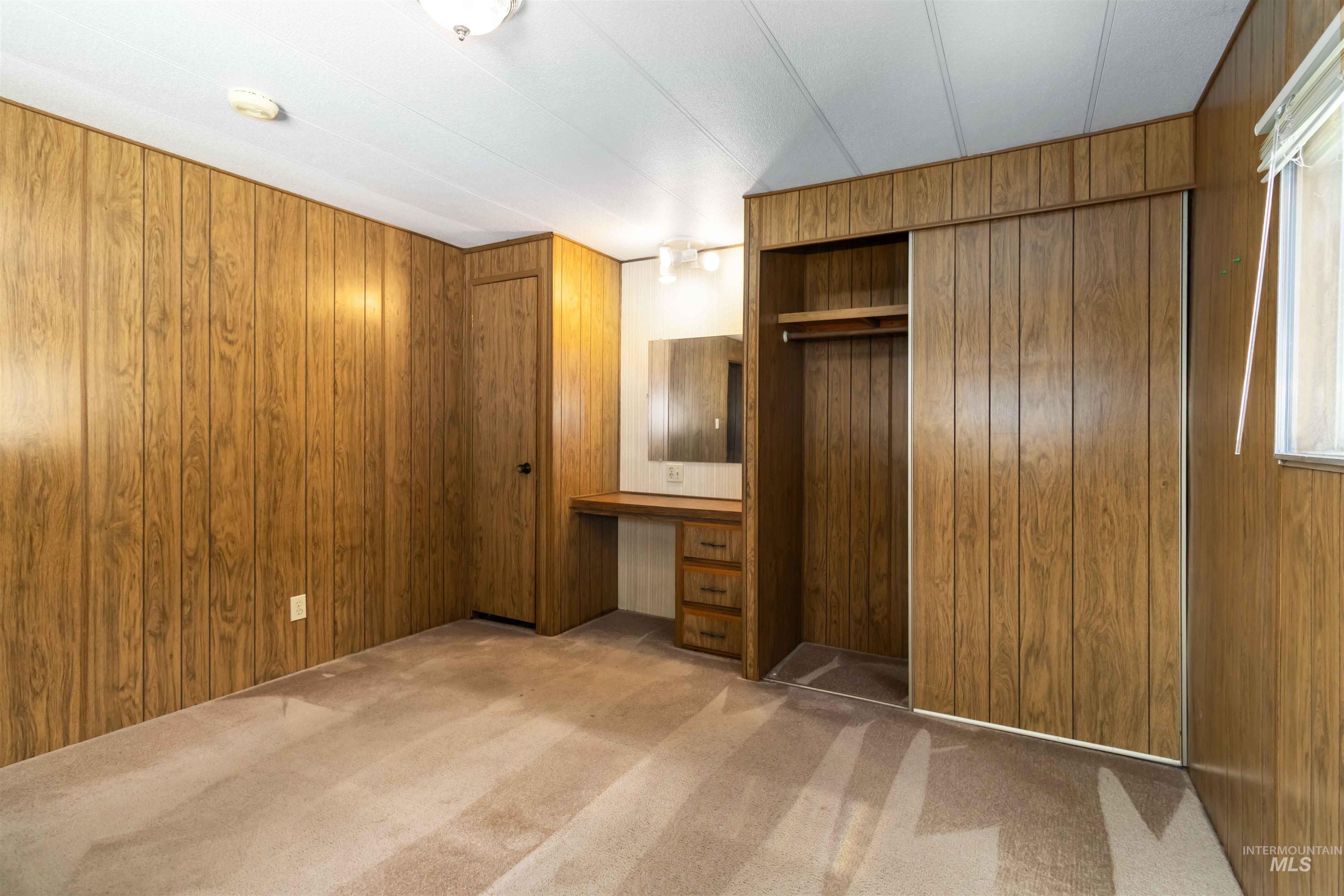 Unfurnished bedroom featuring built in study area, wooden walls, and light carpet