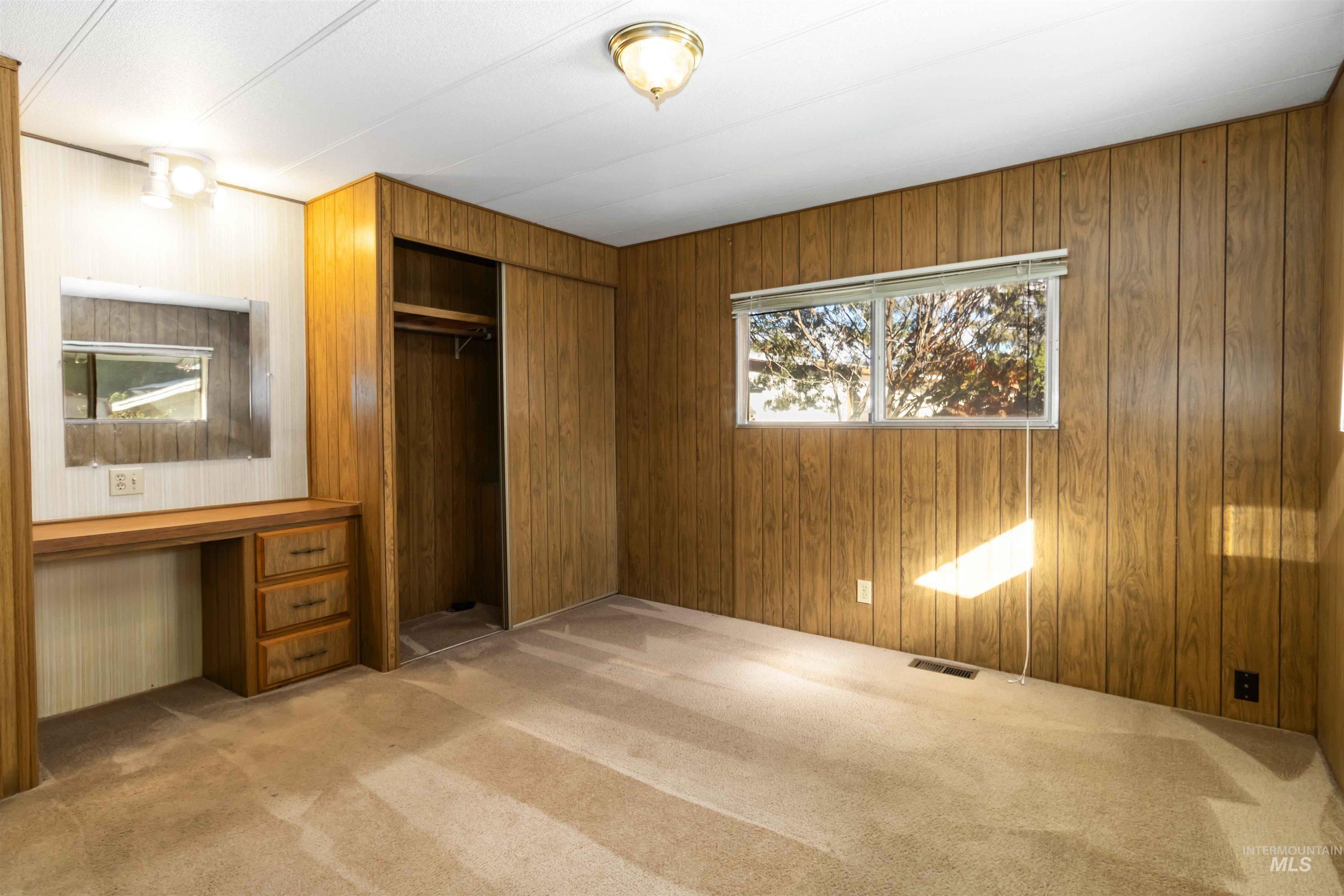 Unfurnished bedroom with light carpet, a closet, wood walls, and built in desk