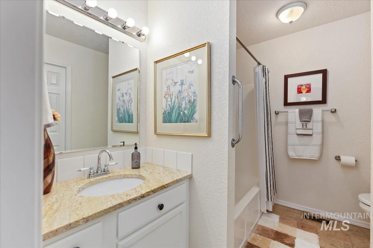 Bathroom with vanity, shower / bath combination with curtain, a textured wall, a textured ceiling, and light tile patterned floors