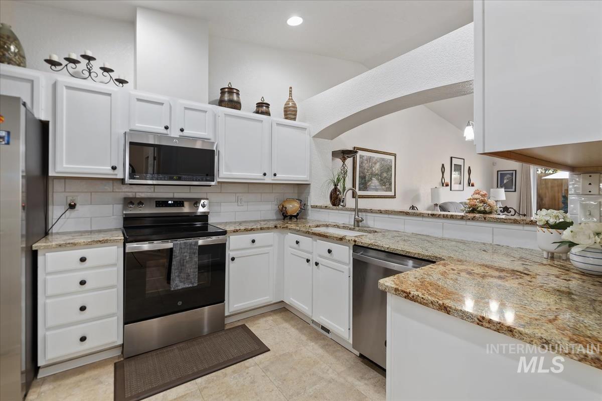 Kitchen with appliances with stainless steel finishes, white cabinetry, tasteful backsplash, and light stone countertops