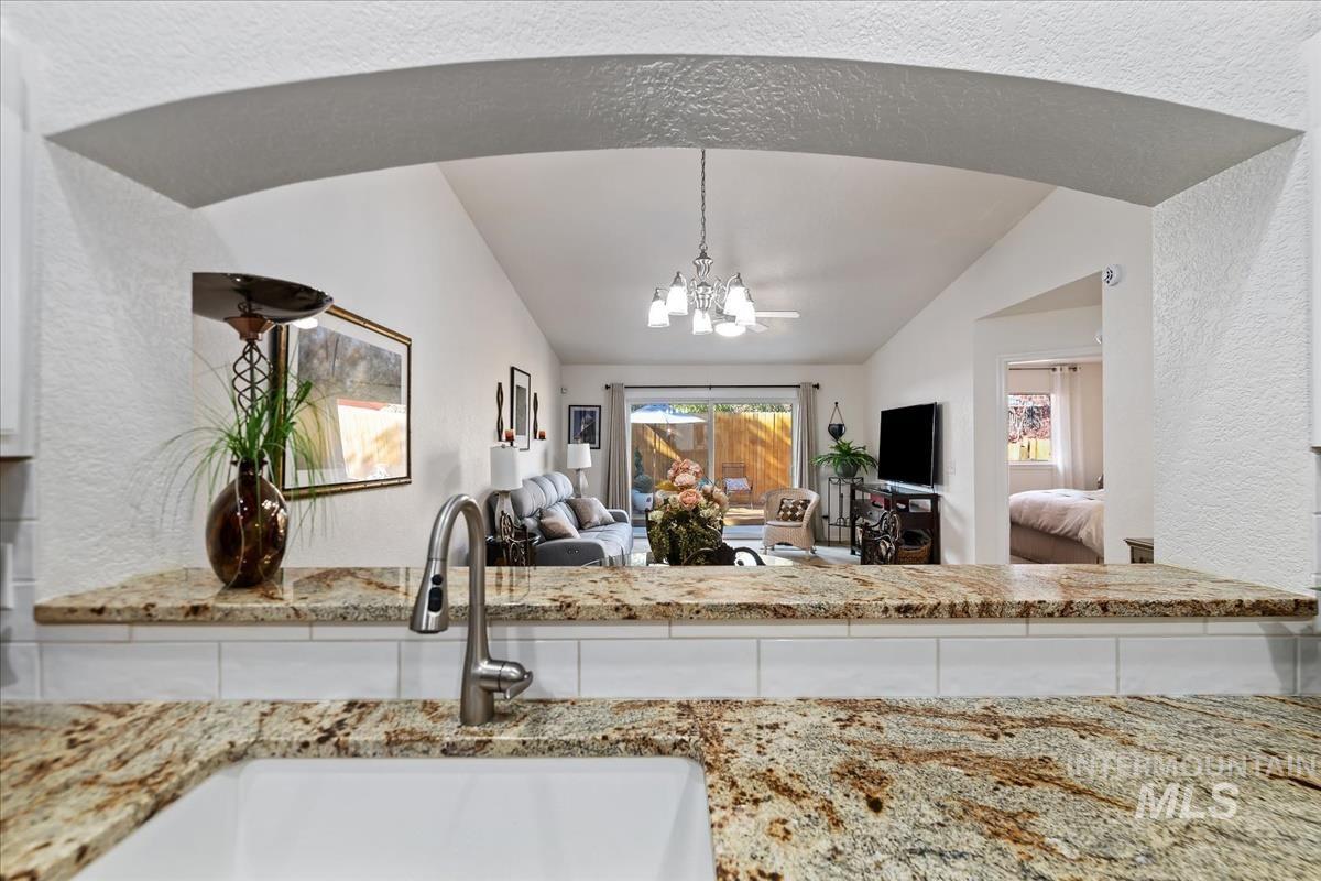 Kitchen with a textured wall, a chandelier, light stone counters, and decorative light fixtures