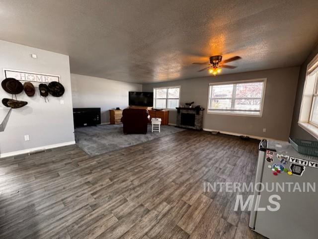 Living area featuring dark wood finished floors, a textured ceiling, ceiling fan, and a fireplace