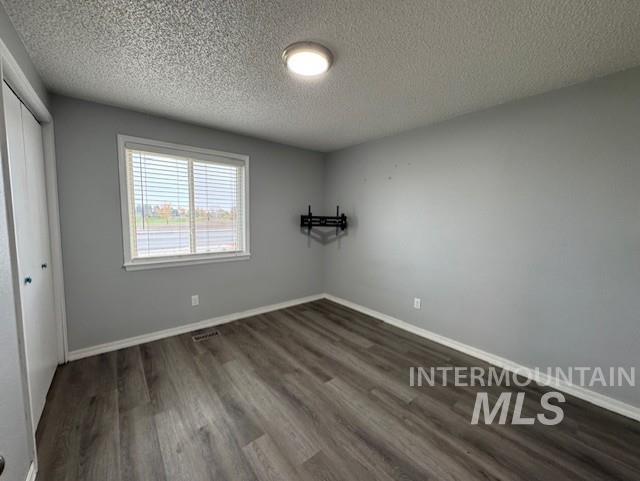Unfurnished bedroom featuring dark wood-style flooring, a closet, and a textured ceiling