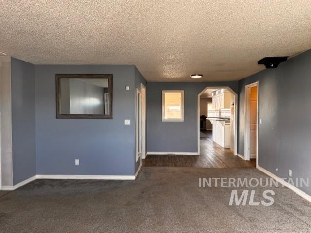 Unfurnished room featuring dark colored carpet, arched walkways, and a textured ceiling