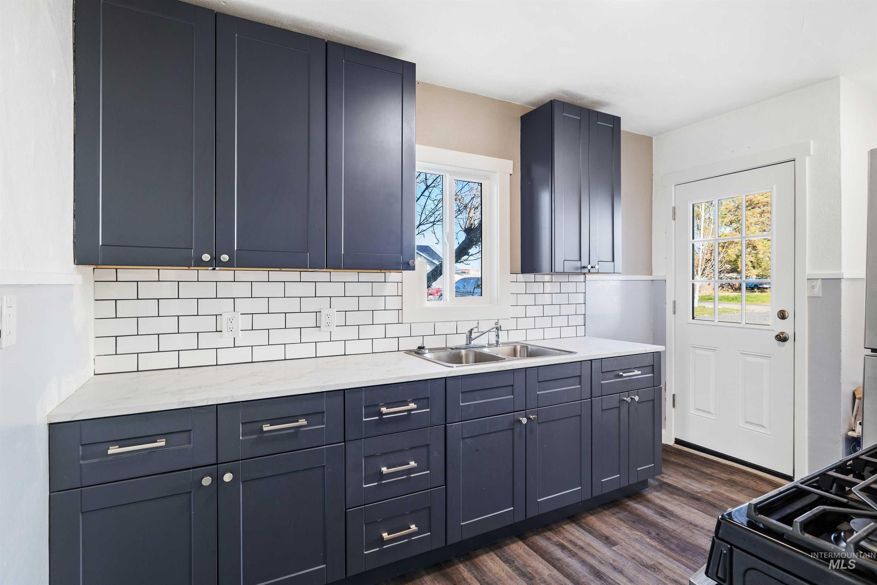 Kitchen with blue cabinetry, dark wood-style flooring, tasteful backsplash, and black gas range