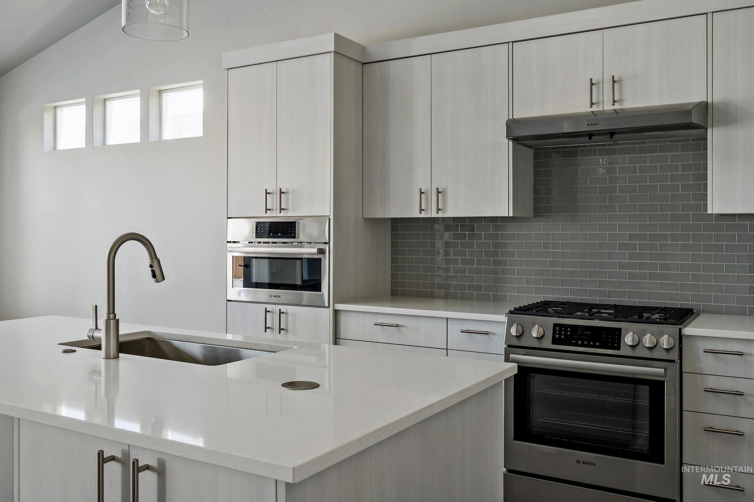 Kitchen with stainless steel appliances, under cabinet range hood, tasteful backsplash, light stone countertops, and vaulted ceiling