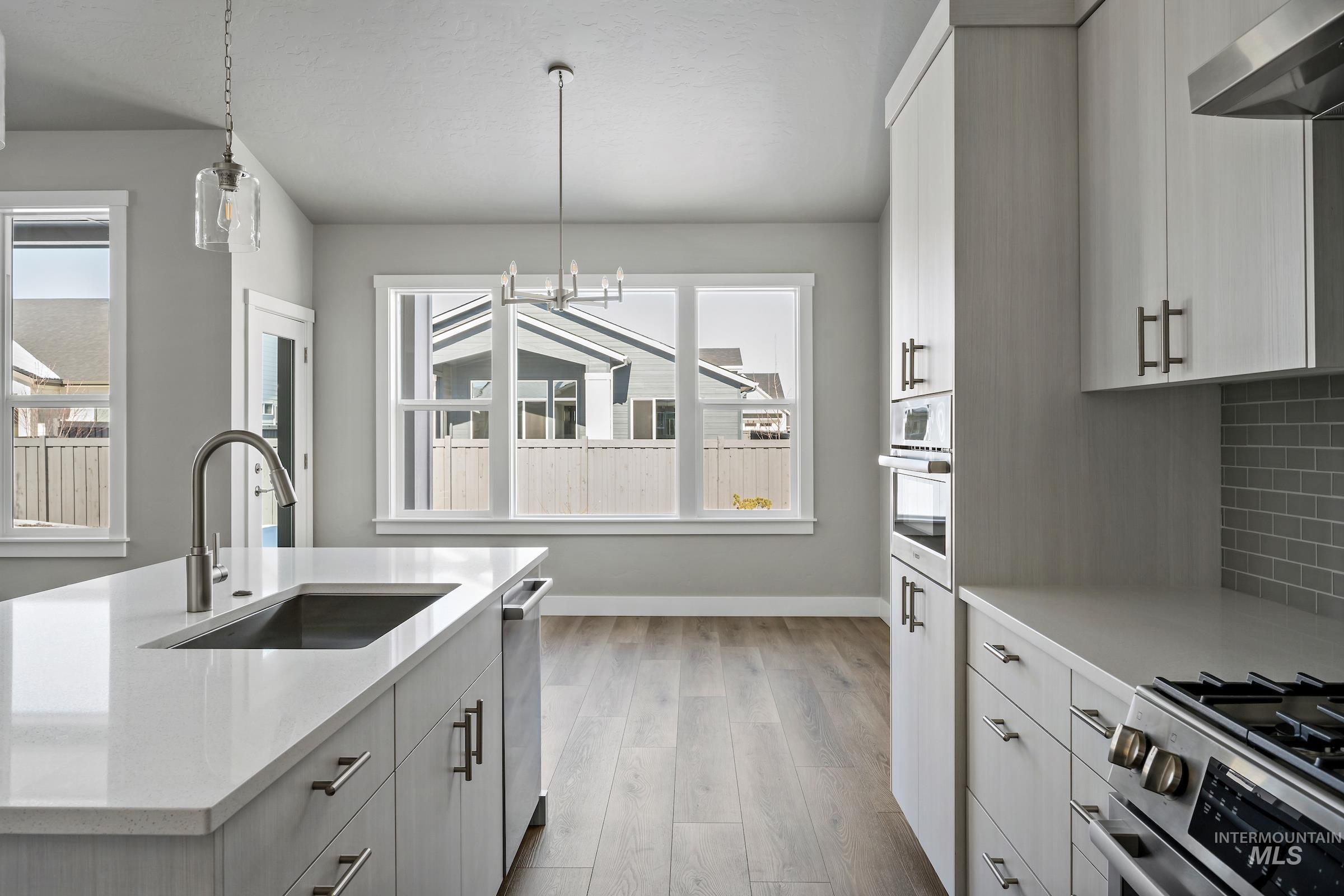 Kitchen with appliances with stainless steel finishes, light wood-type flooring, ventilation hood, white cabinets, and tasteful backsplash