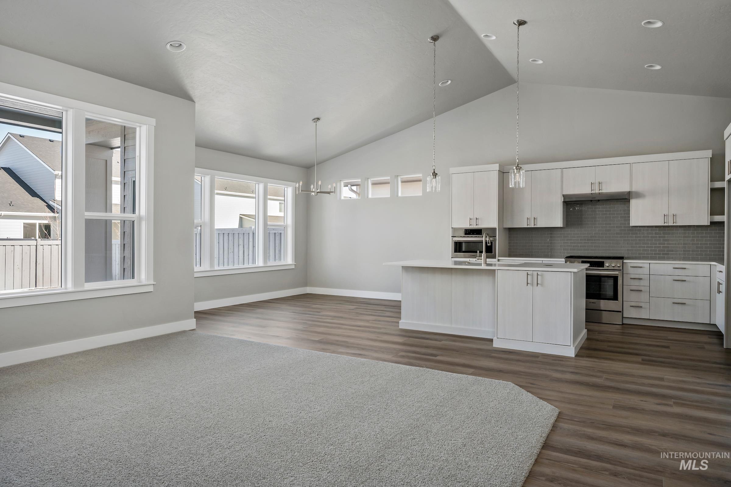 Kitchen featuring white cabinetry, decorative backsplash, high vaulted ceiling, hanging light fixtures, and stainless steel appliances