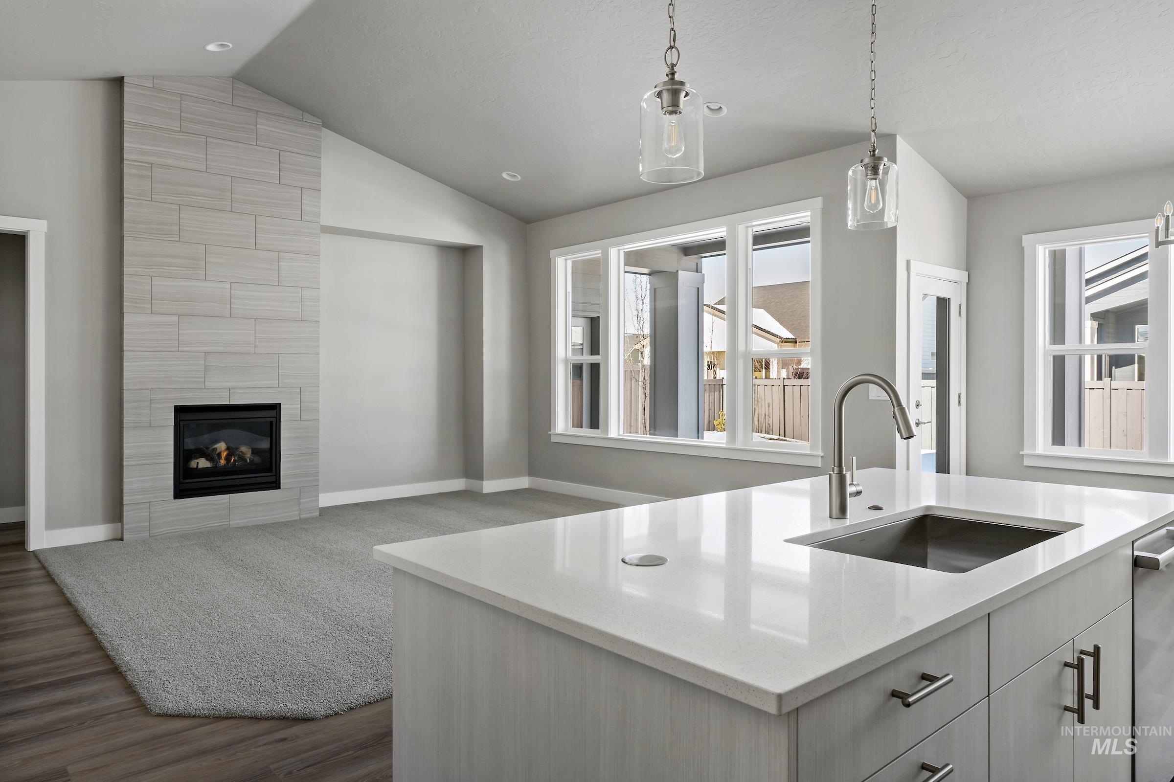 Kitchen with decorative light fixtures, a fireplace, light stone counters, dark wood-type flooring, and vaulted ceiling
