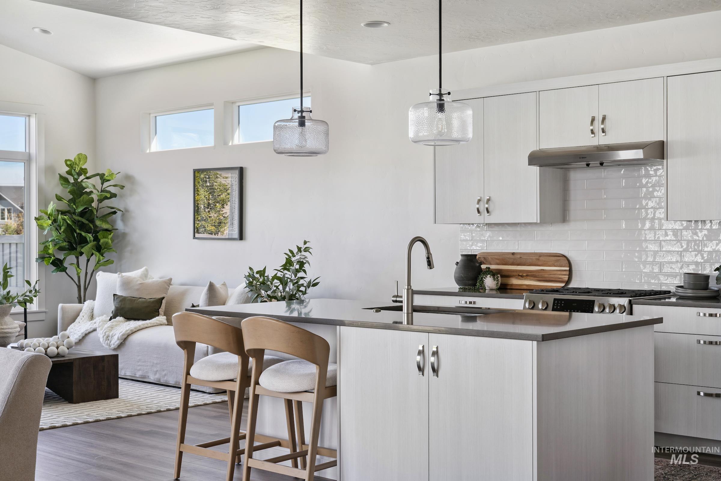 Kitchen with decorative light fixtures, backsplash, dark wood-style flooring, a kitchen breakfast bar, and an island with sink