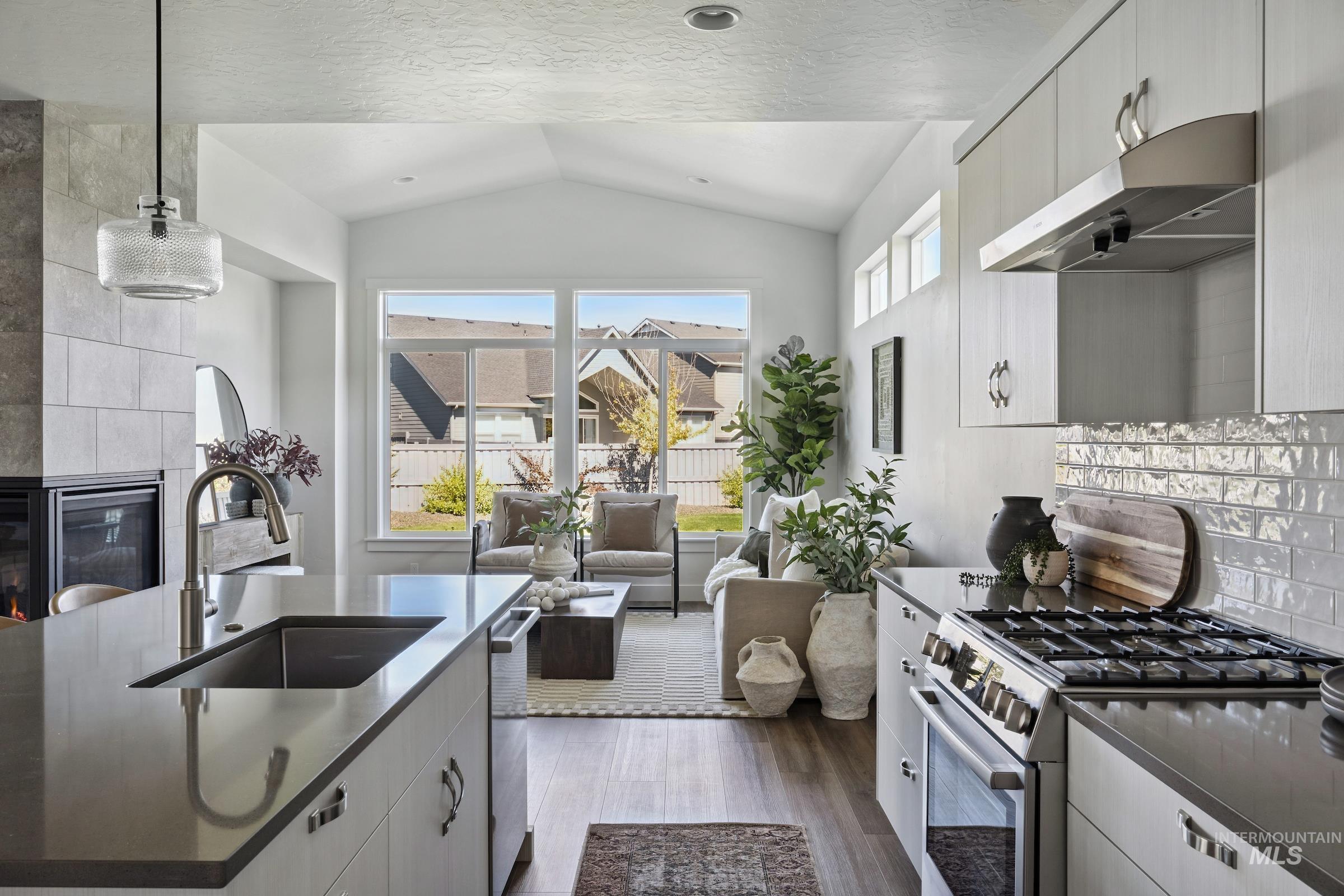 Kitchen featuring tasteful backsplash, appliances with stainless steel finishes, dark wood-style floors, pendant lighting, and under cabinet range hood