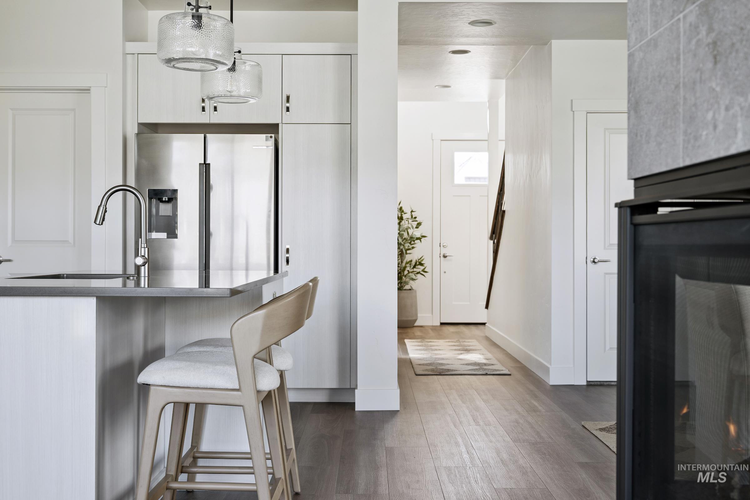 Kitchen with stainless steel fridge with ice dispenser, a lit fireplace, hanging light fixtures, a breakfast bar, and dark wood finished floors