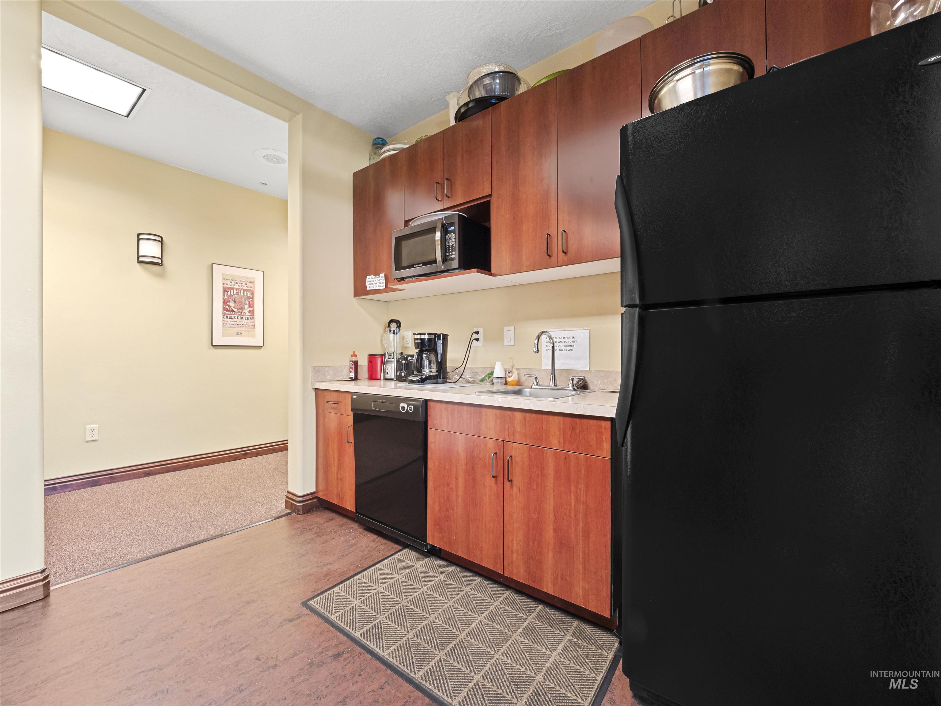 Kitchen featuring black appliances, light countertops, dark wood-type flooring, and brown cabinets