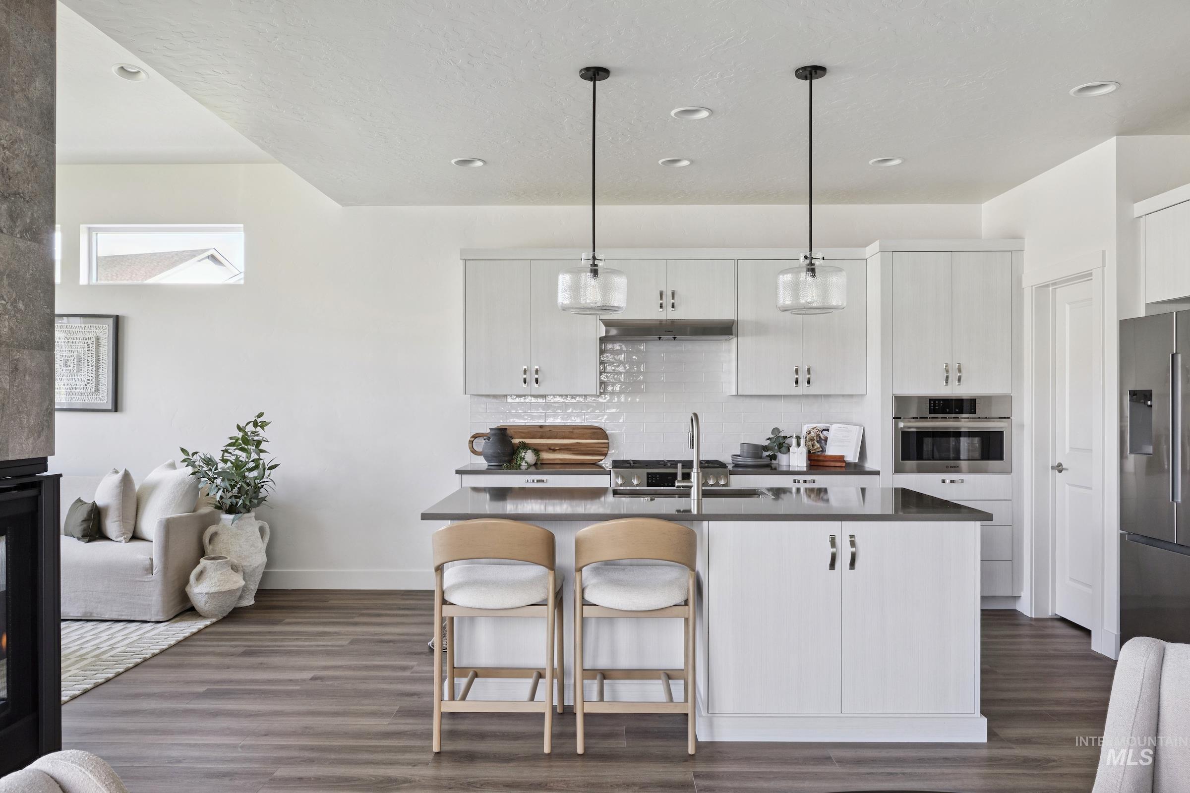 Kitchen with a kitchen island with sink, appliances with stainless steel finishes, pendant lighting, a breakfast bar, and dark wood-style flooring