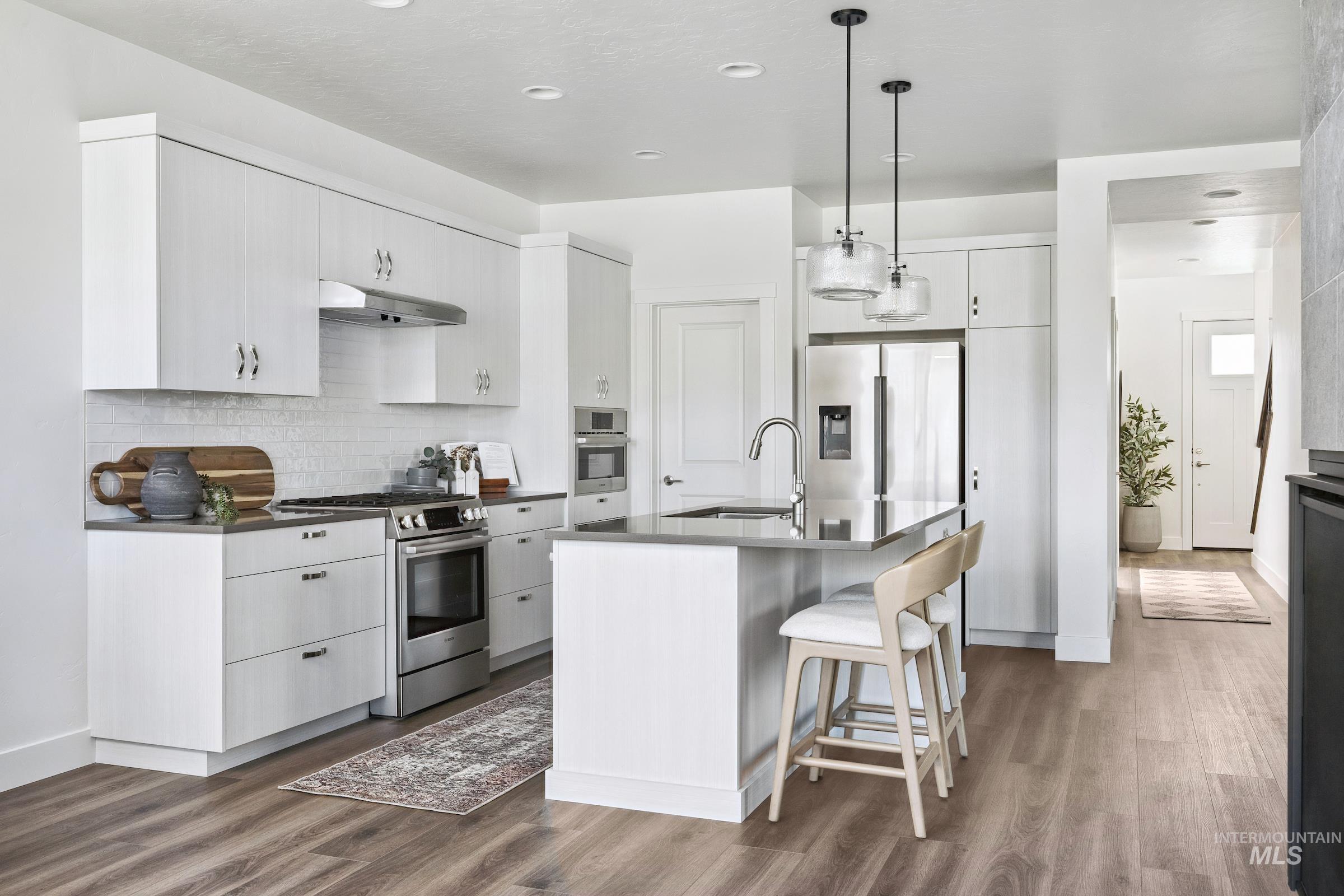 Kitchen with decorative light fixtures, appliances with stainless steel finishes, a kitchen breakfast bar, dark wood-style floors, and decorative backsplash
