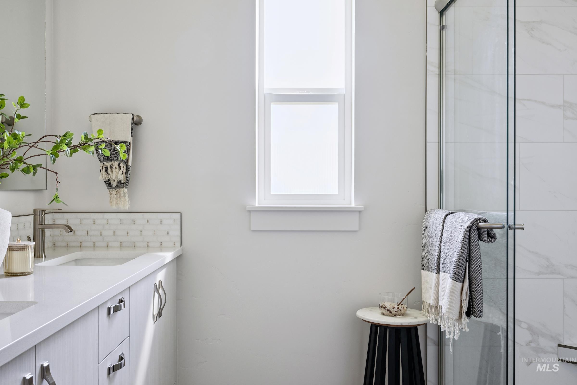 Bathroom with double vanity, backsplash, and a marble finish shower