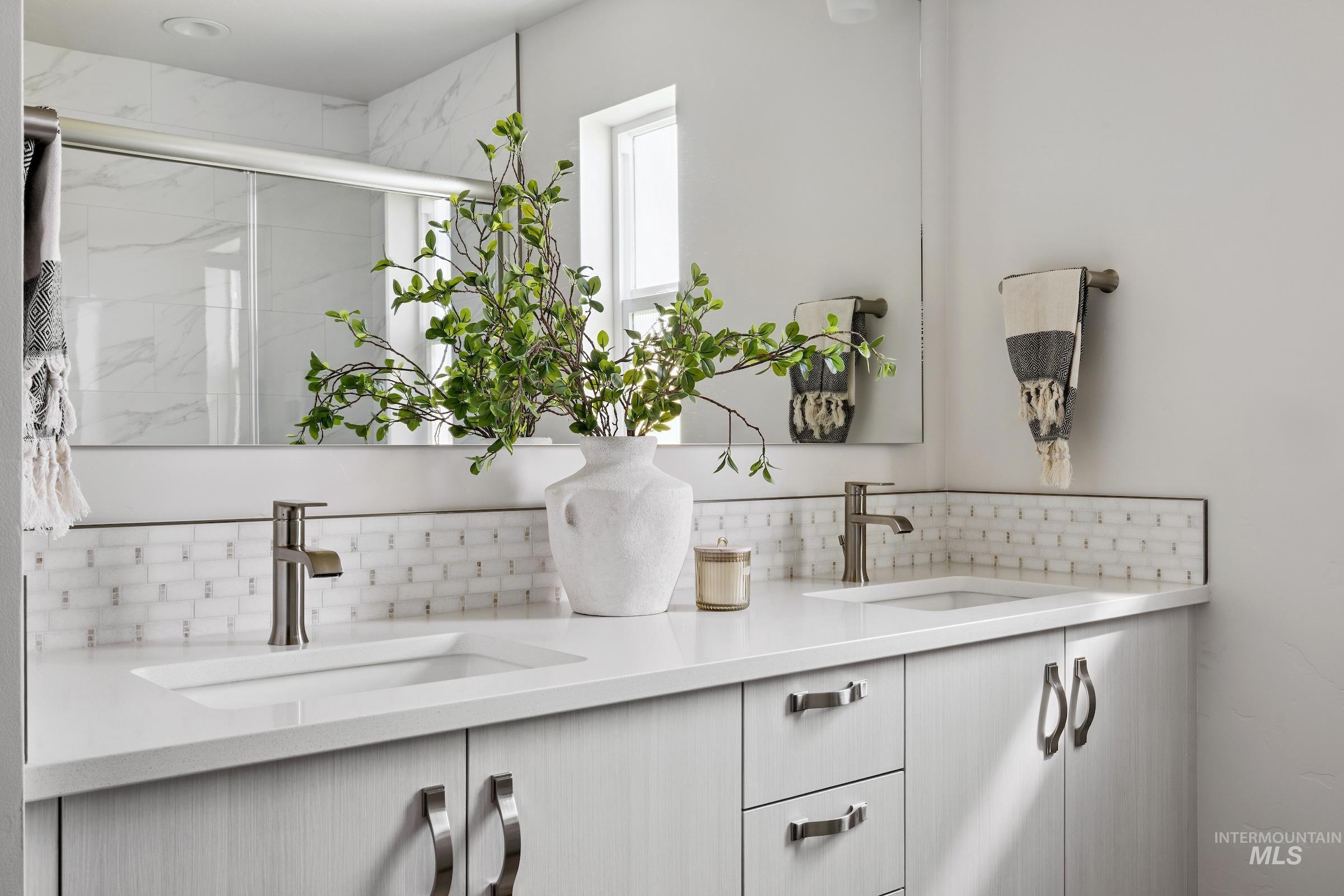 Full bath with a marble finish shower, double vanity, and tasteful backsplash