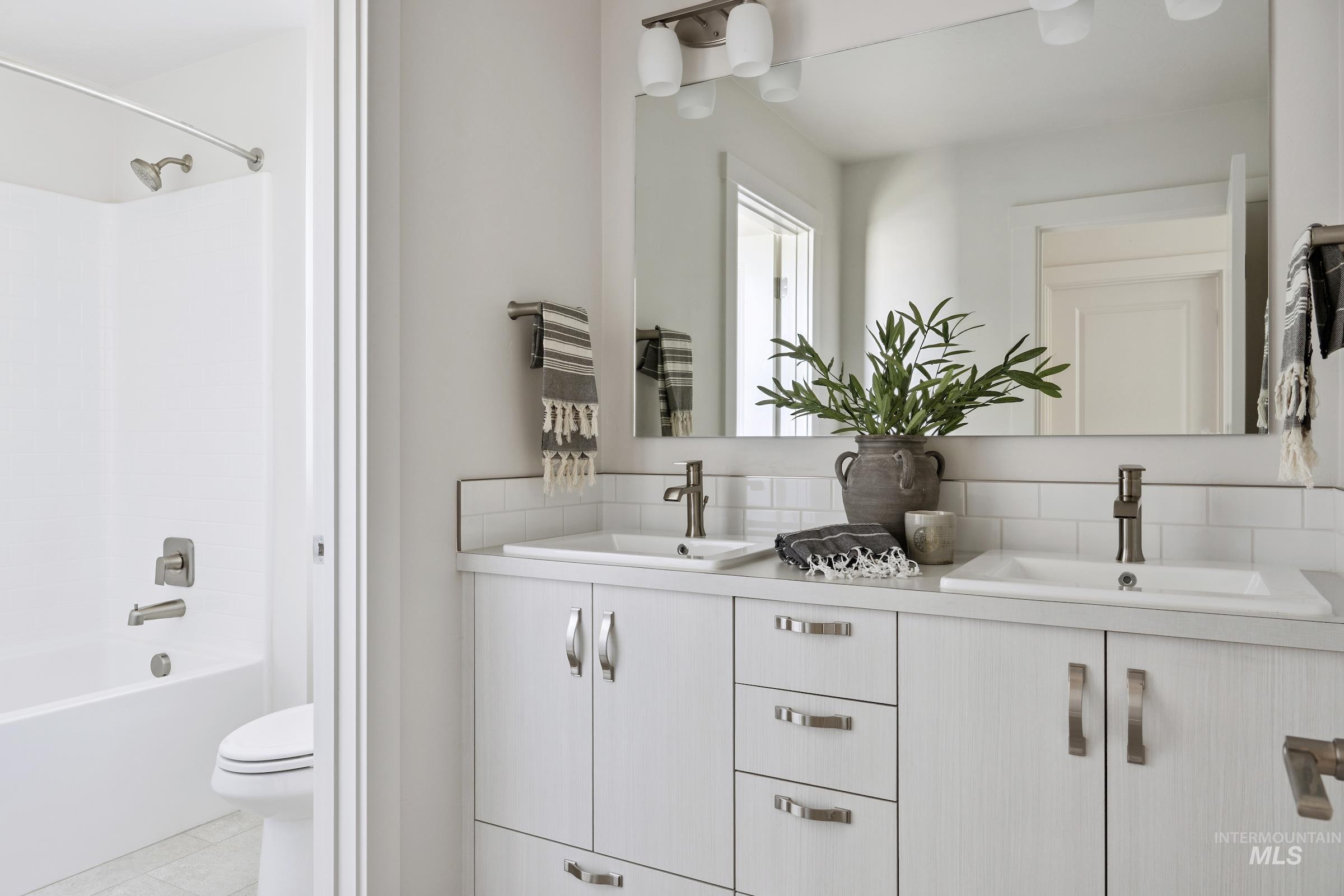 Bathroom with double vanity, shower / washtub combination, tasteful backsplash, and light tile patterned flooring