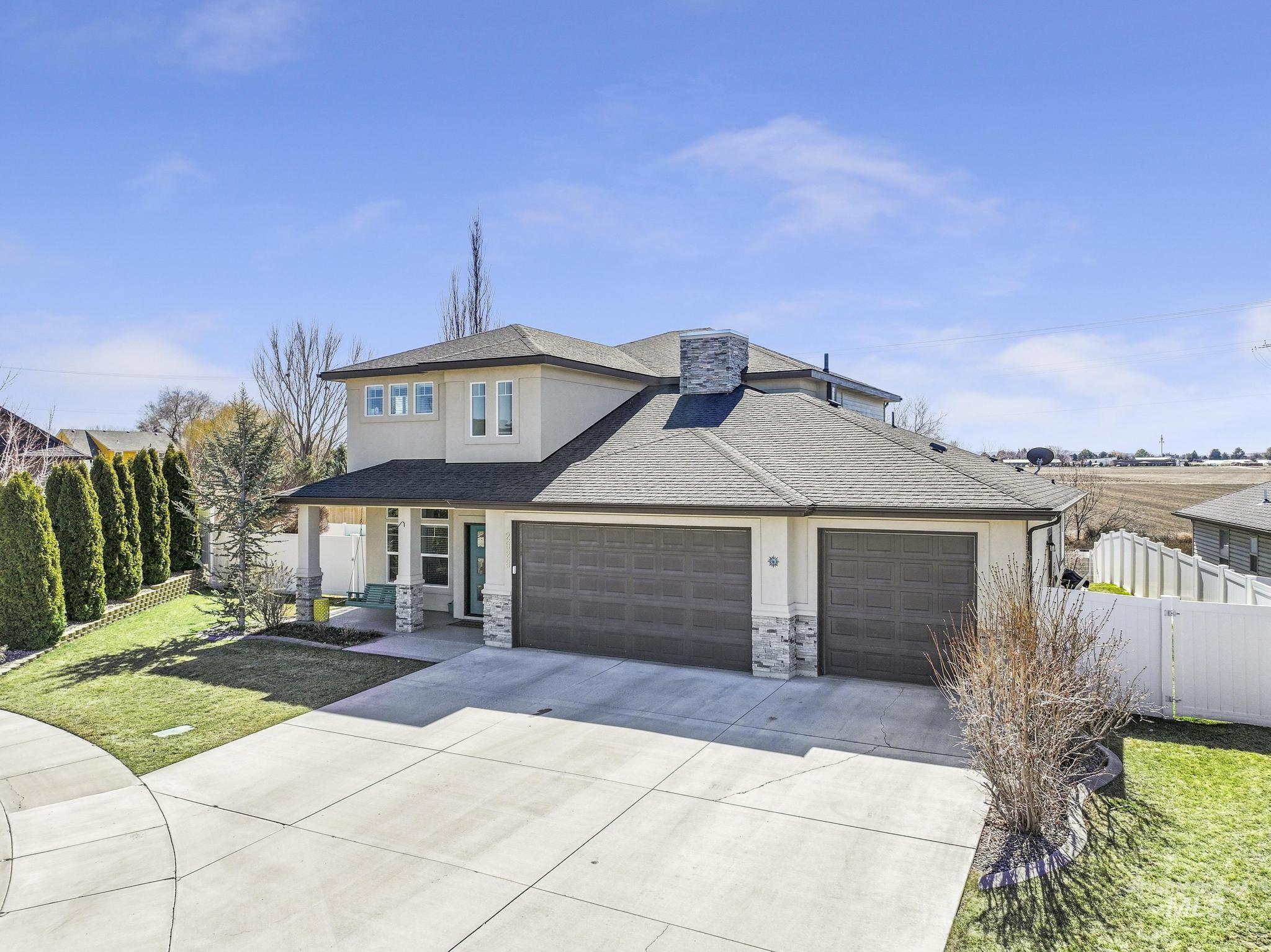 View of front facade with driveway, stucco siding, a shingled roof, covered porch, and an attached garage