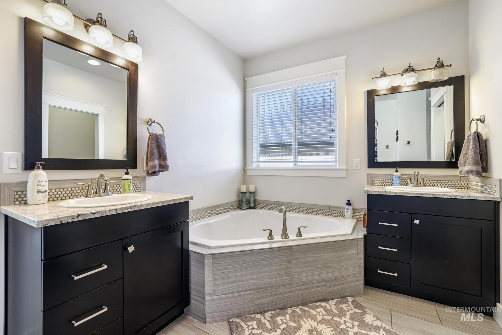 Full bathroom with two vanities, a garden tub, and light wood finished floors