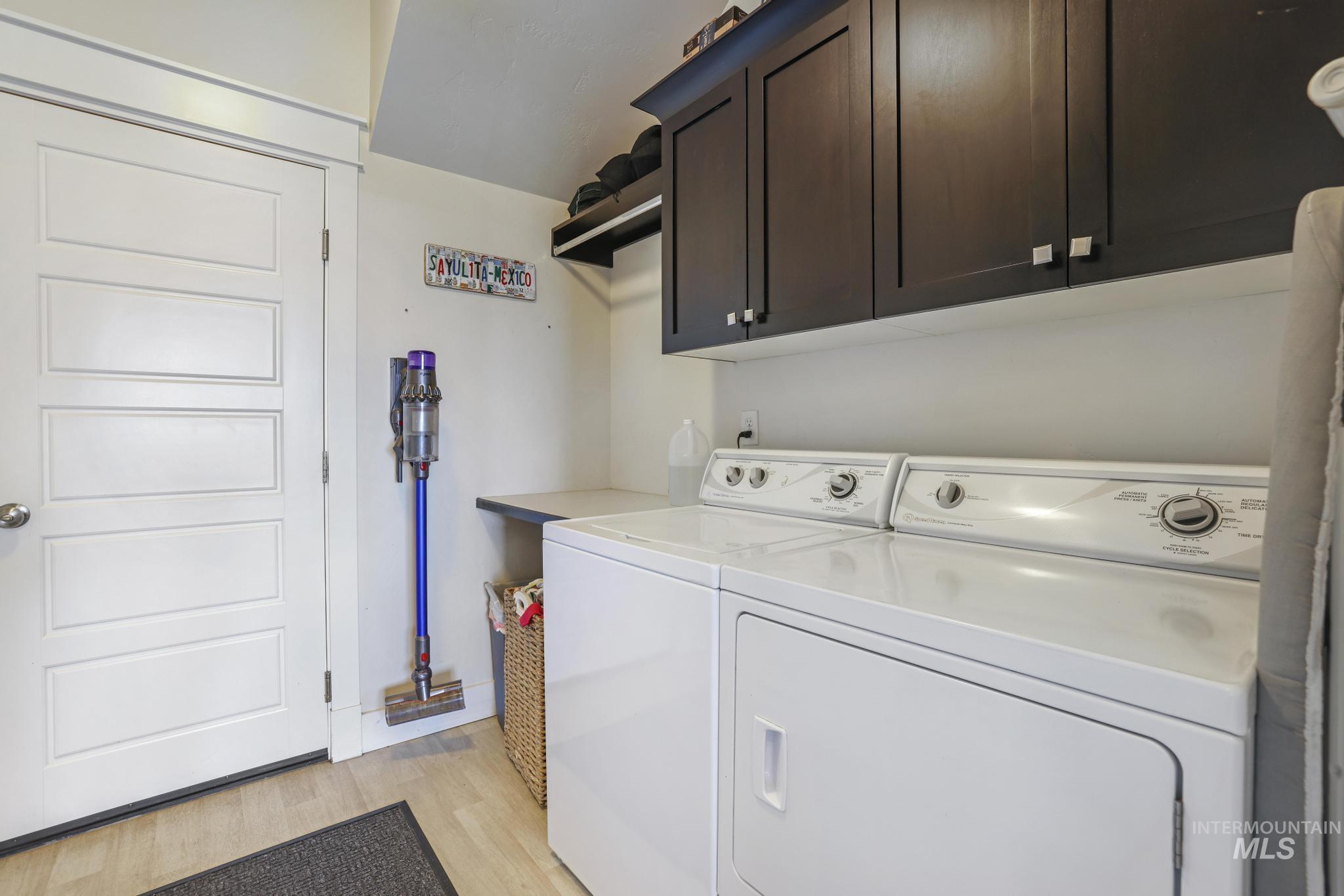 Laundry area with light wood-type flooring, cabinet space, and washer and clothes dryer