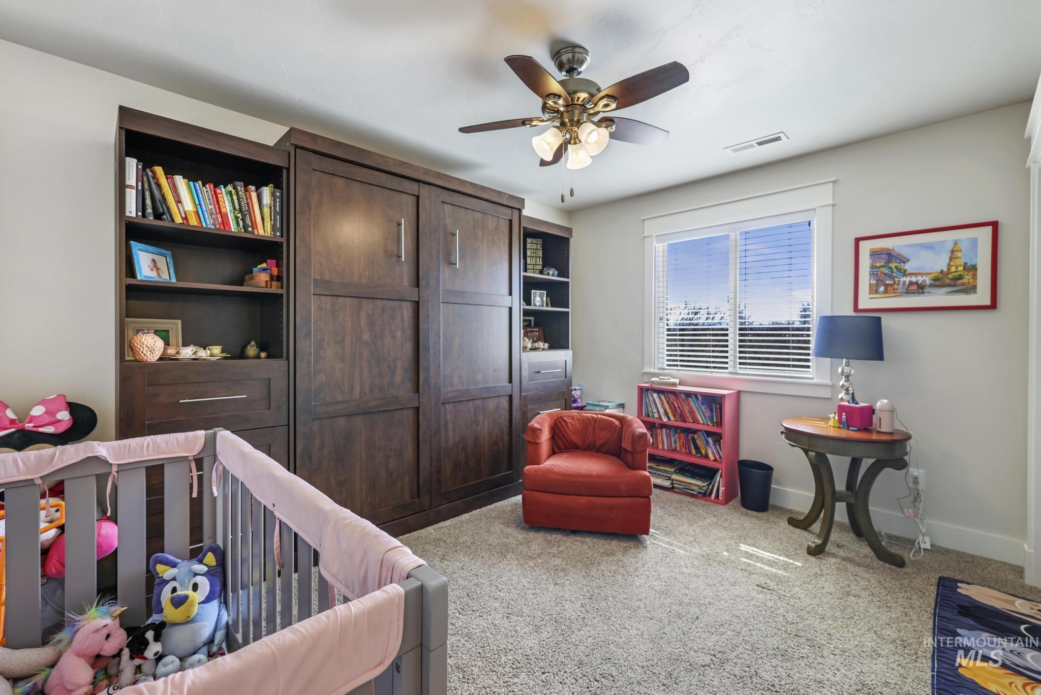 Bedroom featuring light carpet, a ceiling fan, and a nursery area
