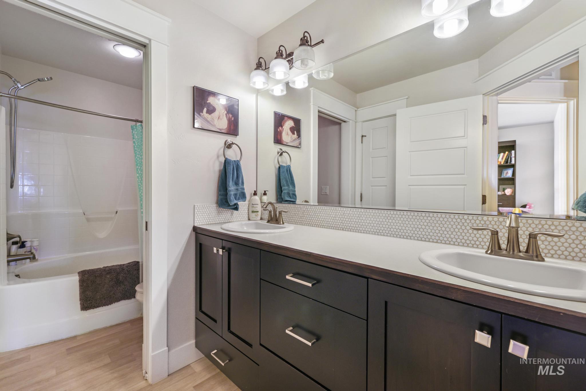 Bathroom with double vanity, shower / bath combo, and light wood finished floors
