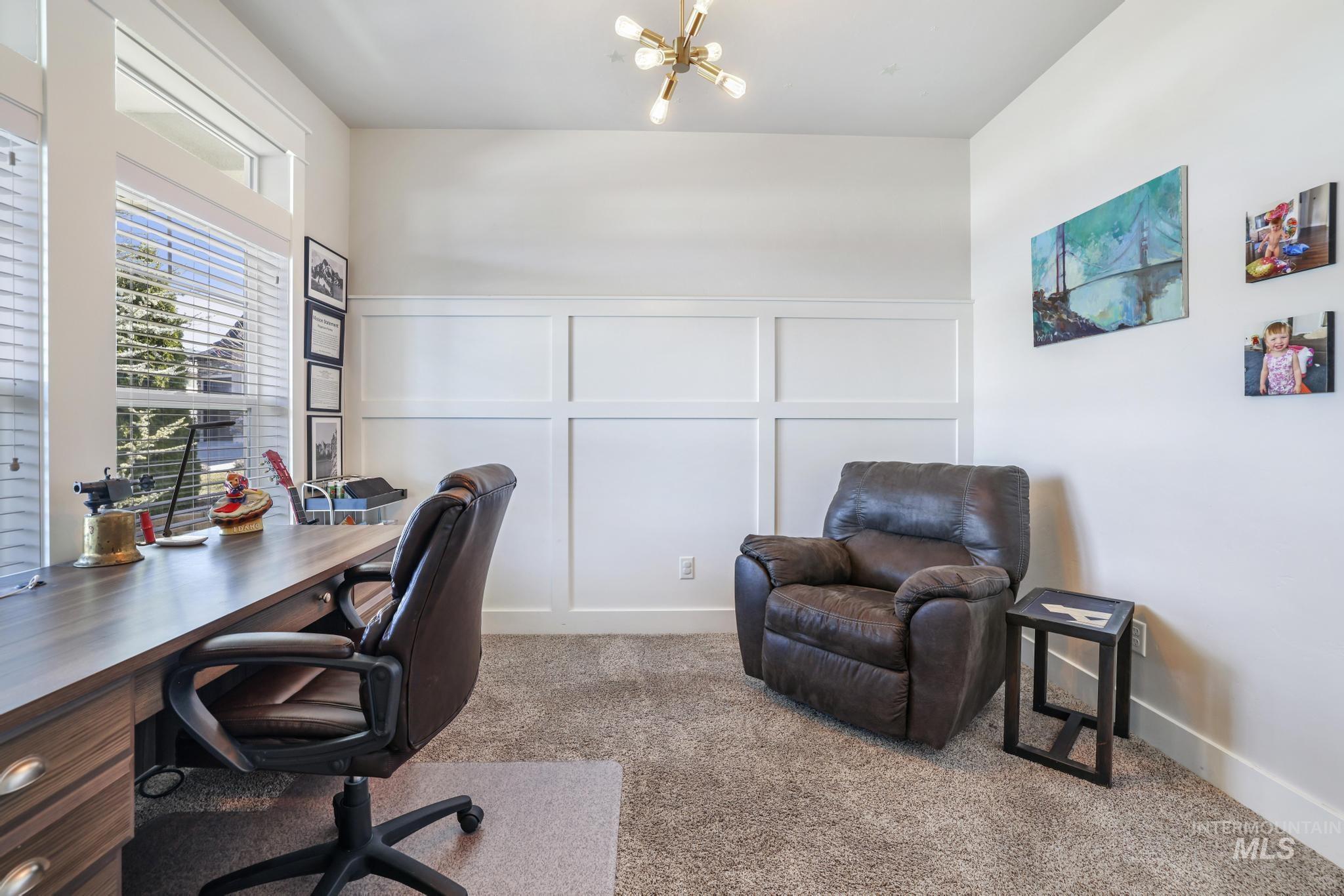 Carpeted home office featuring a decorative wall and a chandelier