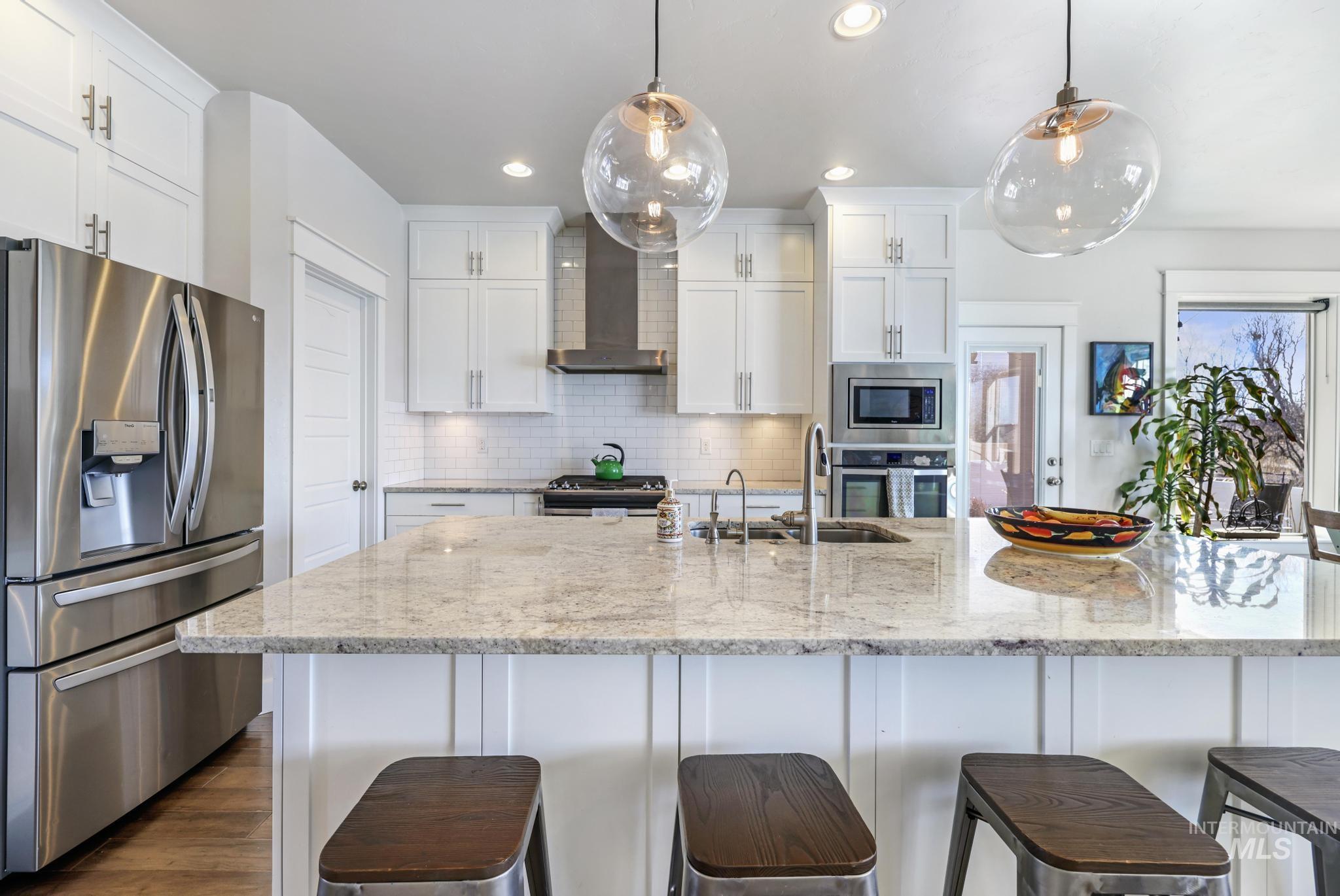 Kitchen with appliances with stainless steel finishes, backsplash, white cabinetry, light stone countertops, and recessed lighting