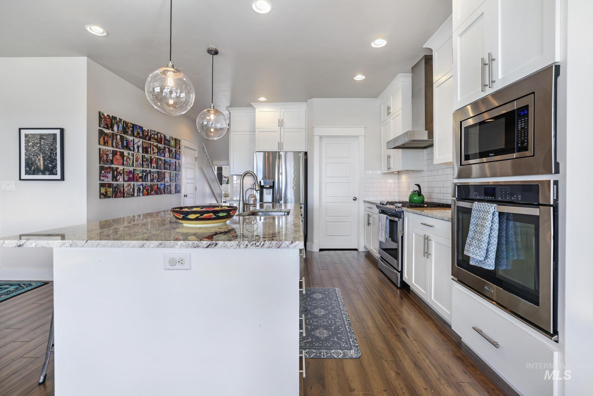 Kitchen with appliances with stainless steel finishes, dark wood-style floors, backsplash, wall chimney exhaust hood, and light stone counters