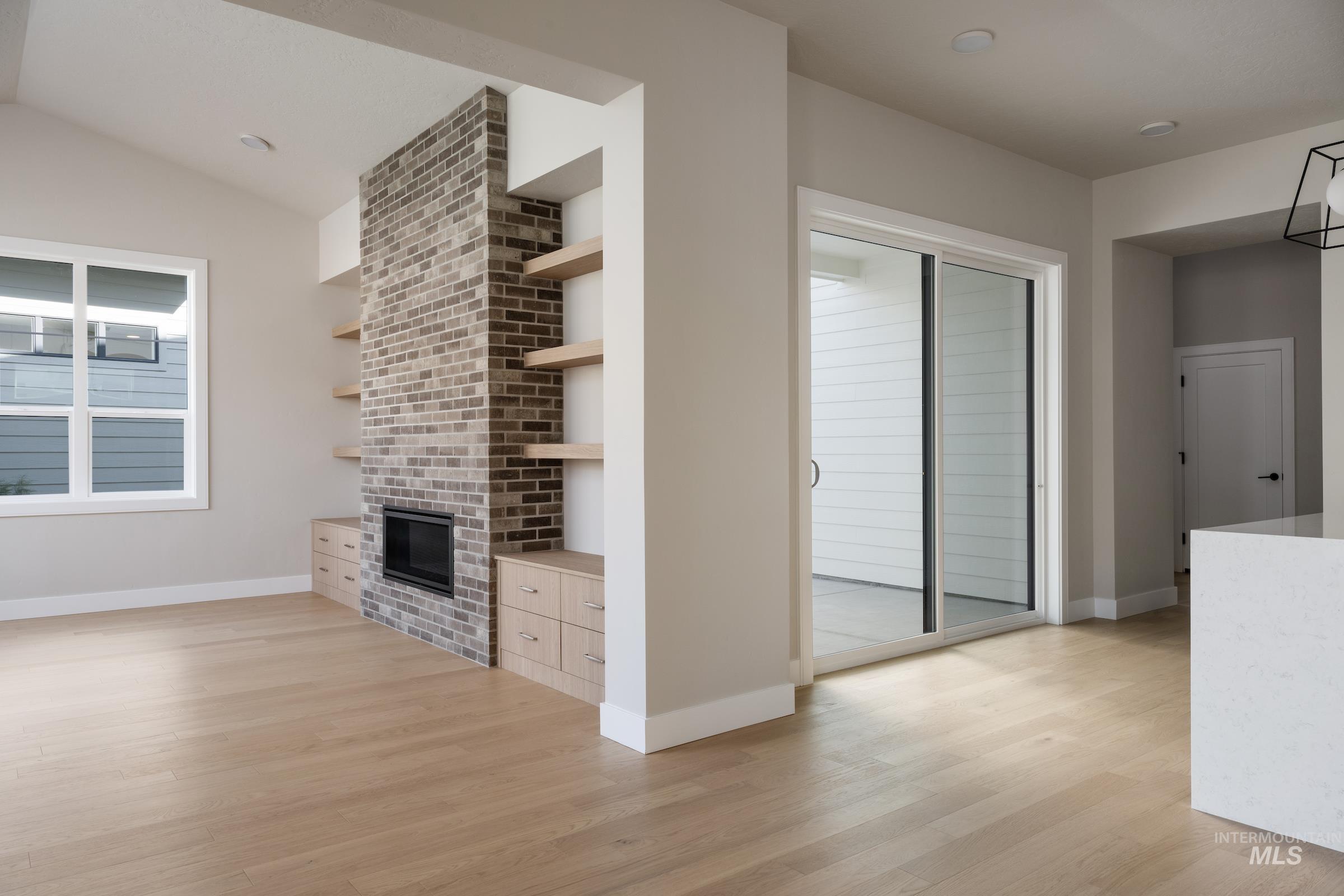 Unfurnished living room featuring light wood-style flooring, a brick fireplace, and lofted ceiling