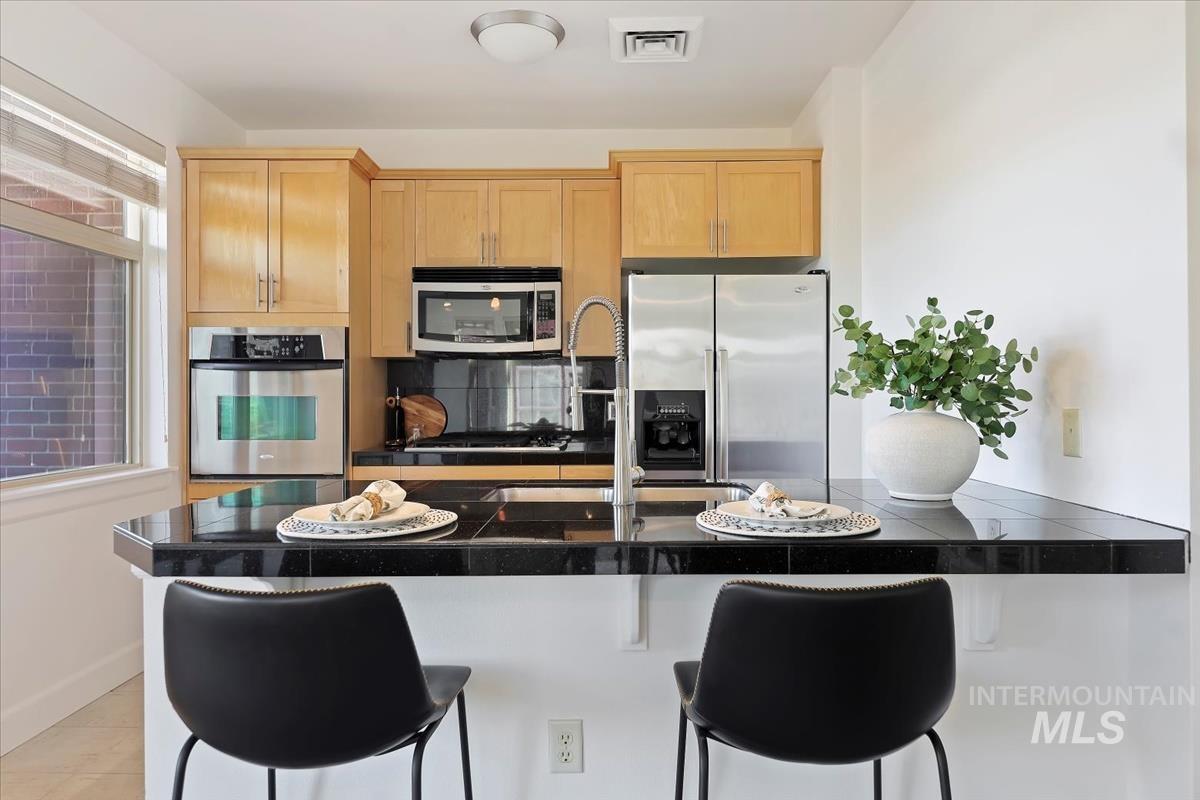 Kitchen with appliances with stainless steel finishes, a breakfast bar, light brown cabinetry, tasteful backsplash, and light tile patterned flooring