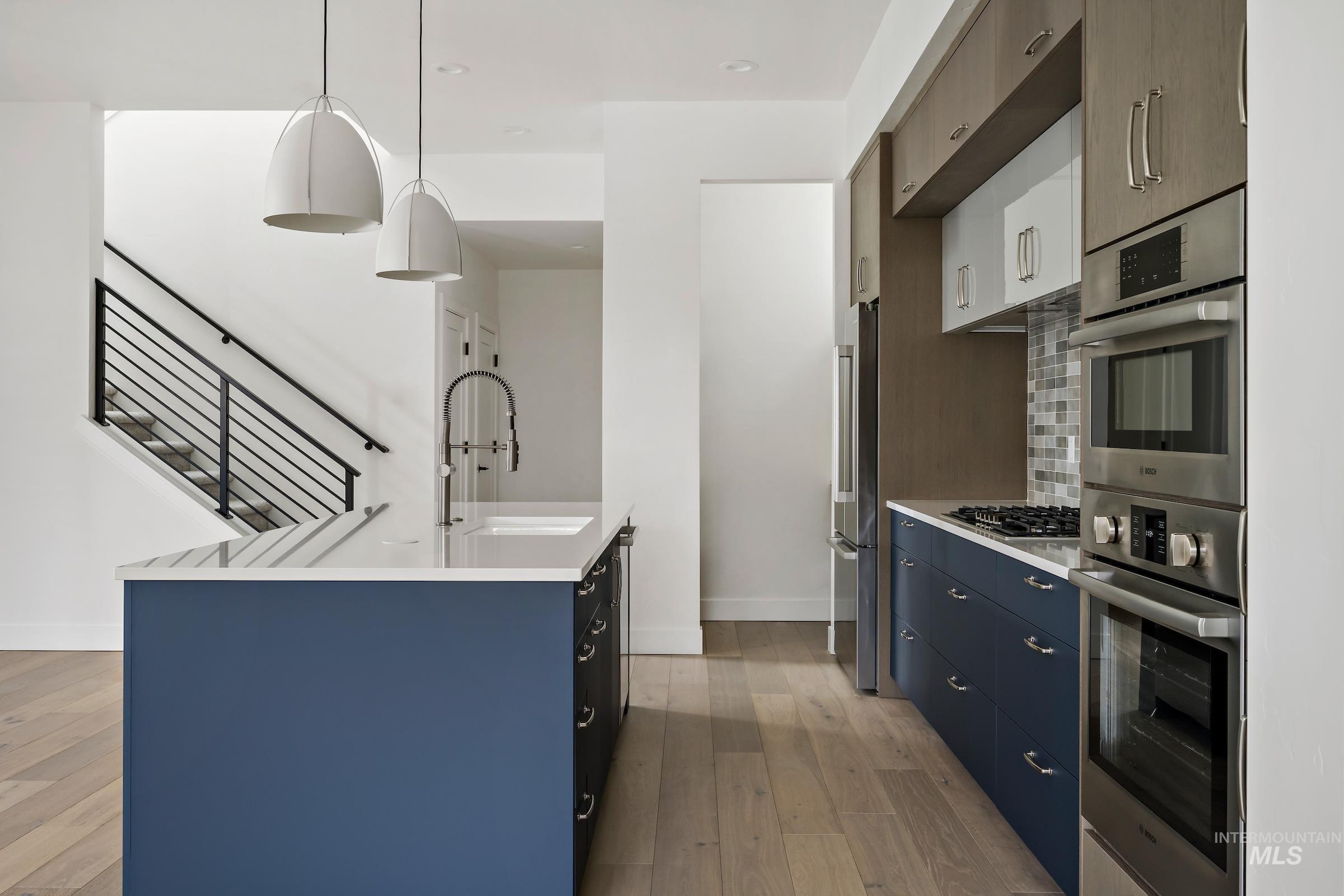 Kitchen with pendant lighting, light wood finished floors, appliances with stainless steel finishes, blue cabinetry, and a kitchen island with sink