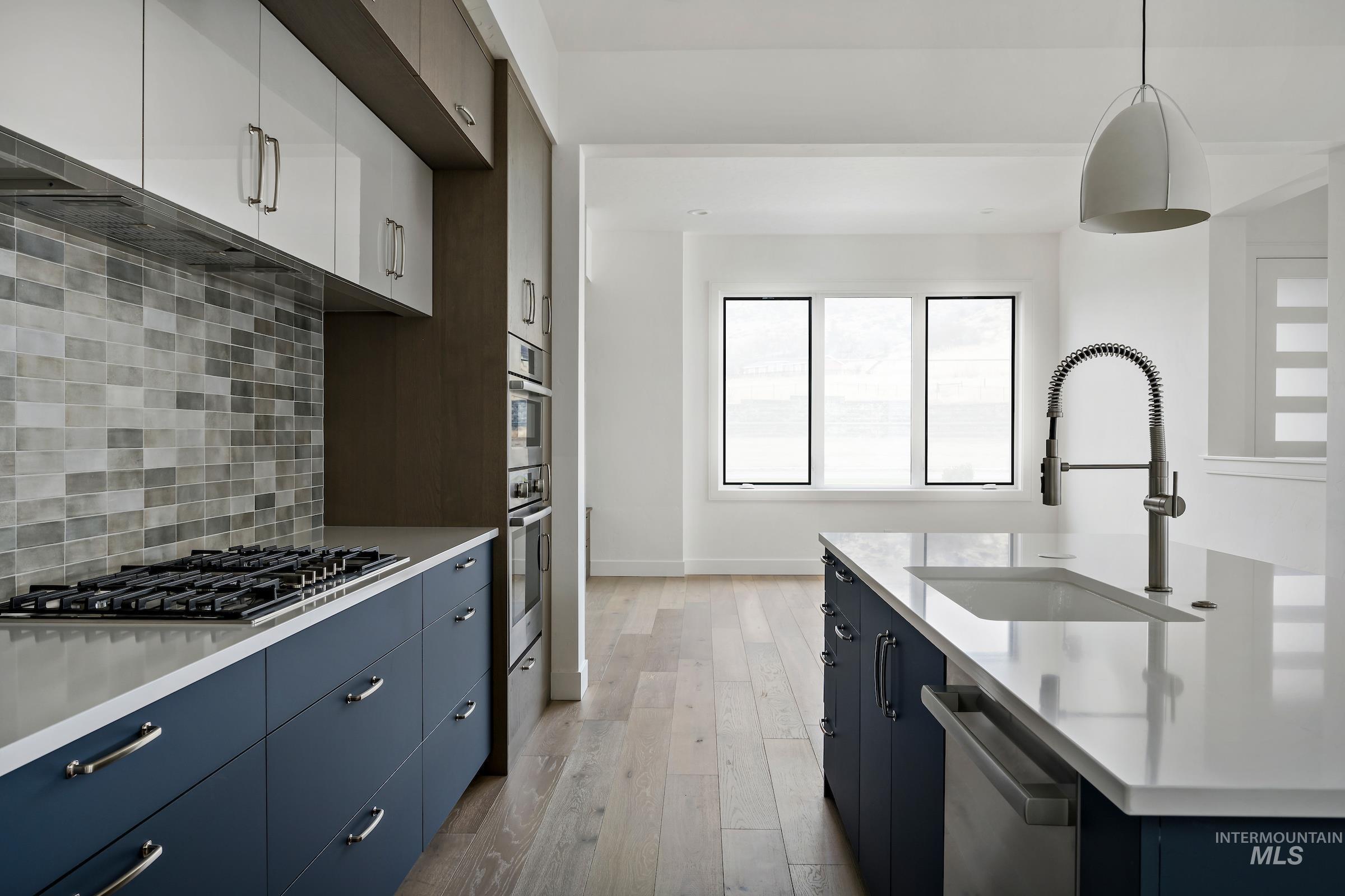 Kitchen featuring tasteful backsplash, decorative light fixtures, light wood-type flooring, stainless steel appliances, and blue cabinetry