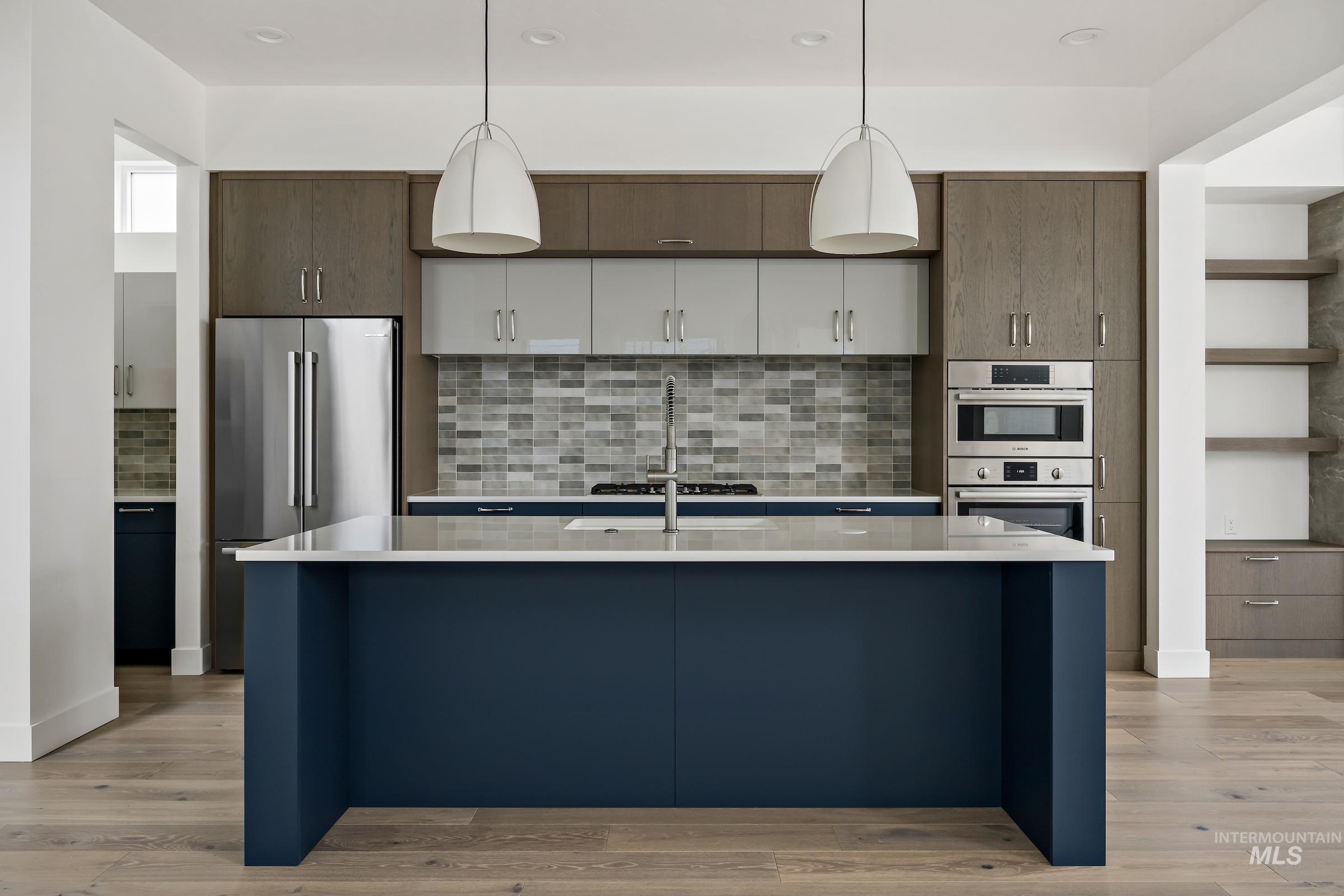 Kitchen featuring stainless steel appliances, decorative light fixtures, a center island with sink, open shelves, and recessed lighting