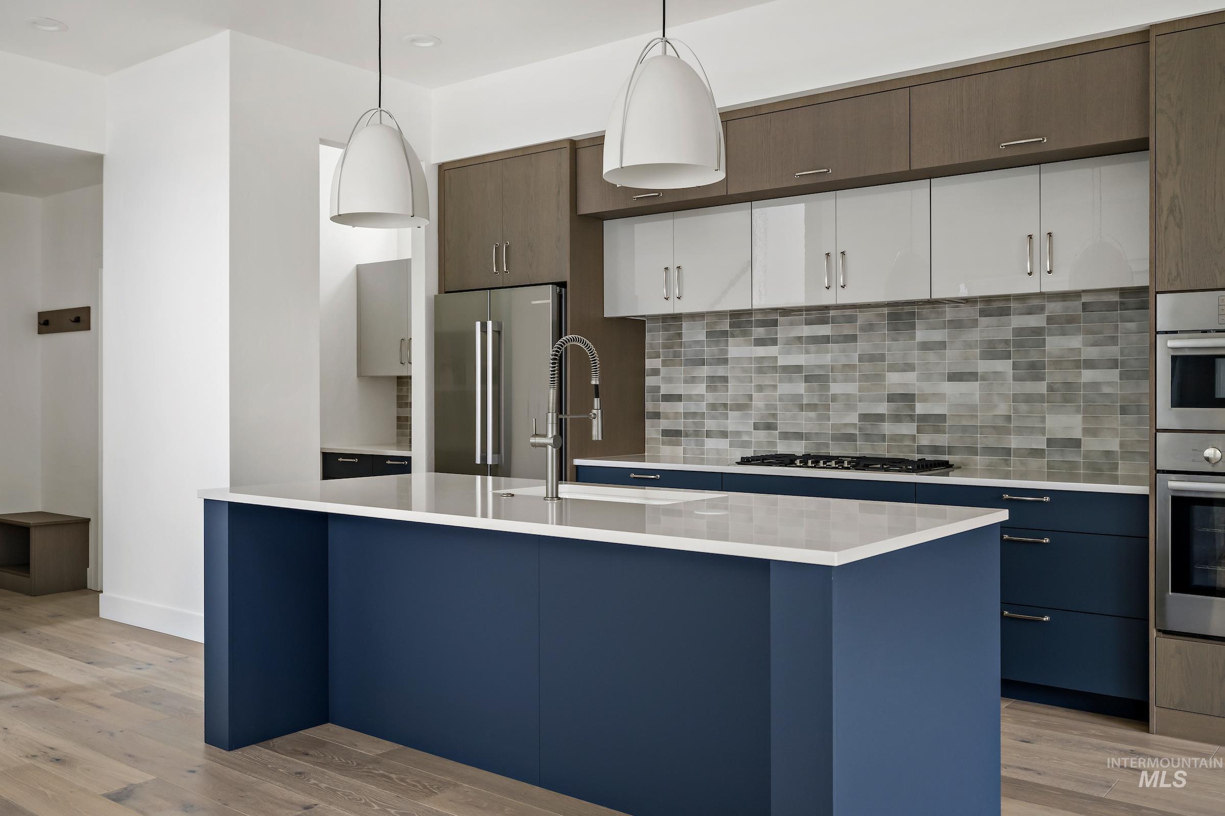 Kitchen with white cabinetry, decorative light fixtures, blue cabinetry, backsplash, and light wood finished floors