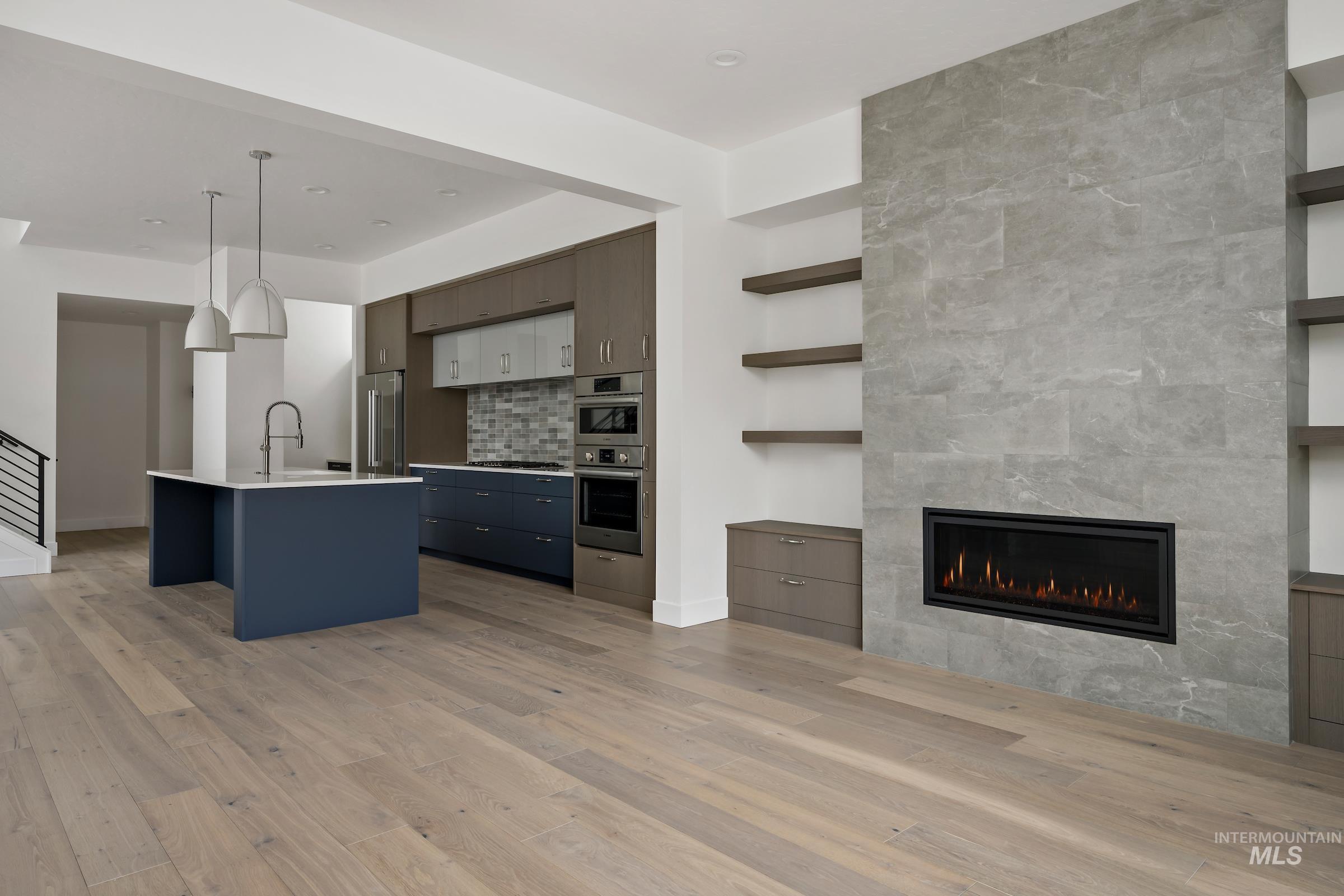 Kitchen featuring decorative light fixtures, light countertops, decorative backsplash, appliances with stainless steel finishes, and light wood-style flooring