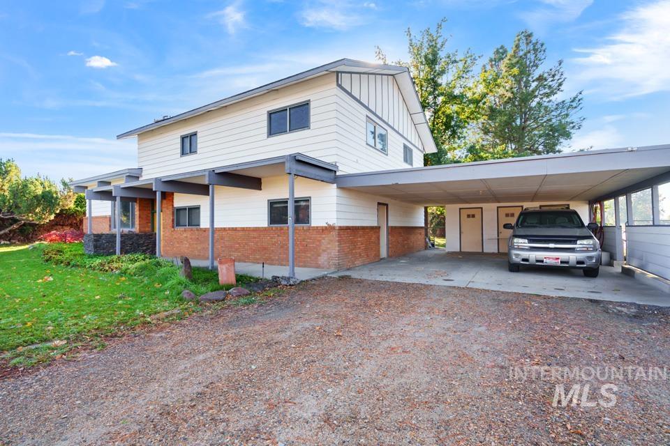 View of front of house featuring brick siding, dirt driveway, an attached carport, and board and batten siding