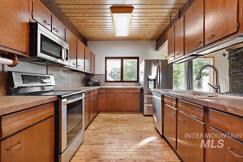 Kitchen featuring stainless steel appliances, brown cabinets, wooden ceiling, backsplash, and light wood-style floors