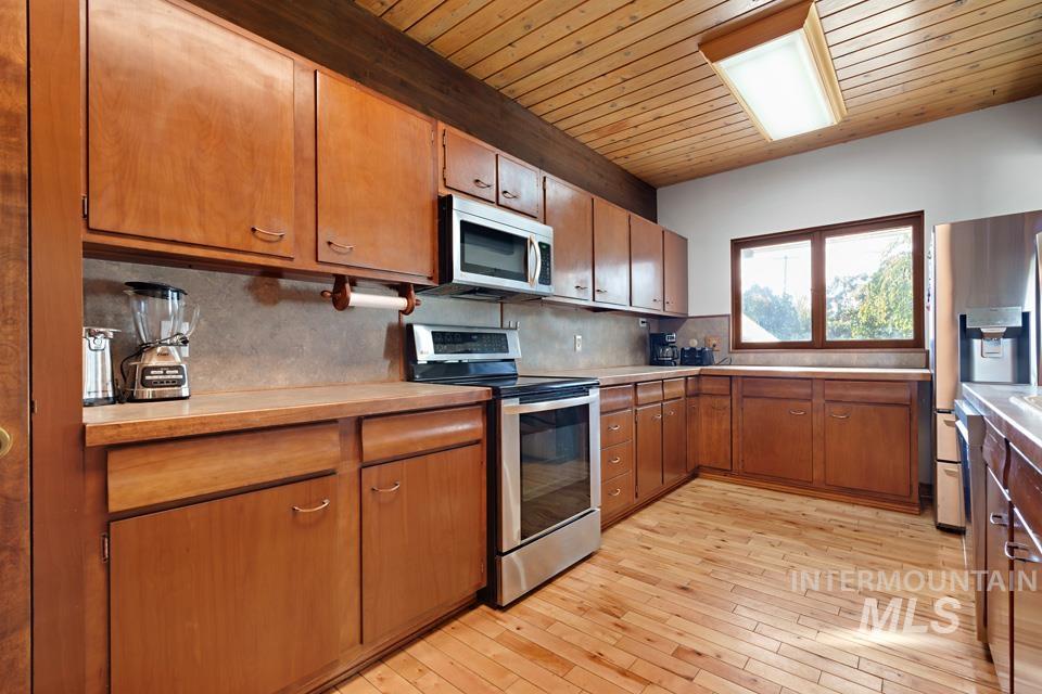 Kitchen featuring appliances with stainless steel finishes, light countertops, light wood-style flooring, tasteful backsplash, and wooden ceiling