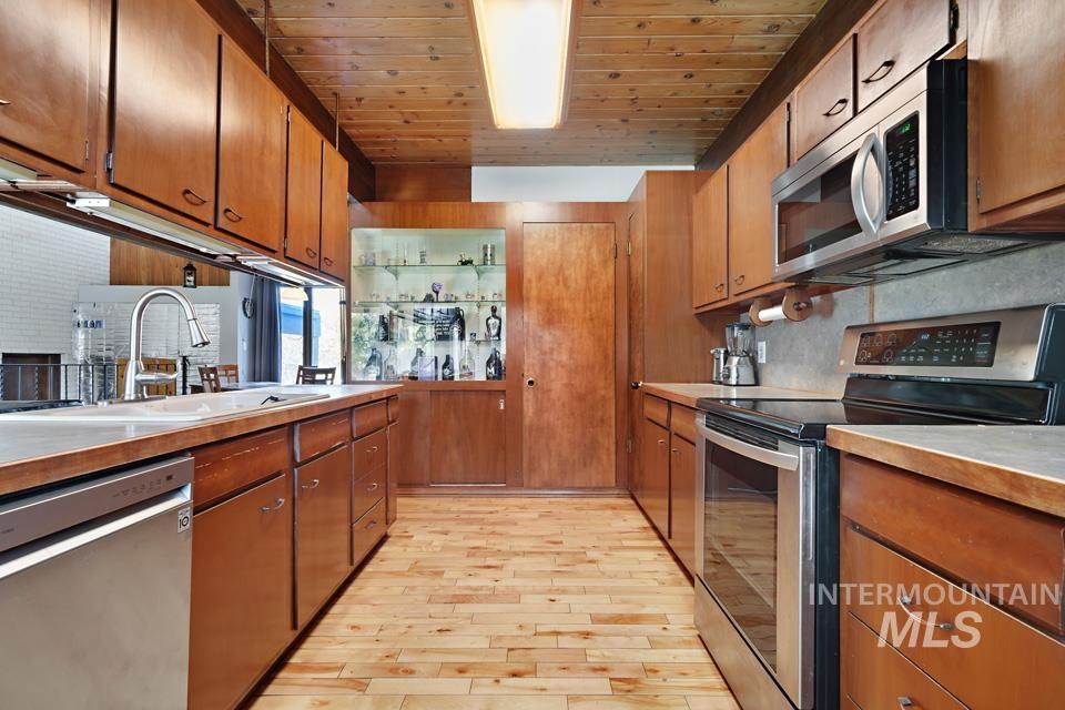 Kitchen featuring stainless steel appliances, light wood-style flooring, wood ceiling, brown cabinetry, and light countertops