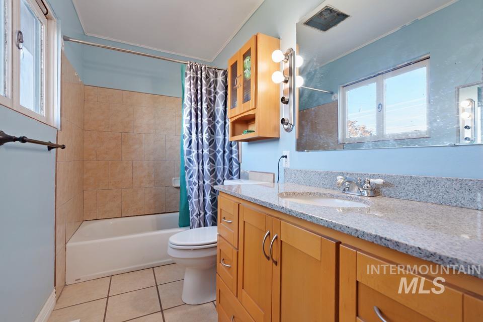 Full bathroom featuring vanity, shower / tub combo with curtain, light tile patterned floors, and healthy amount of natural light