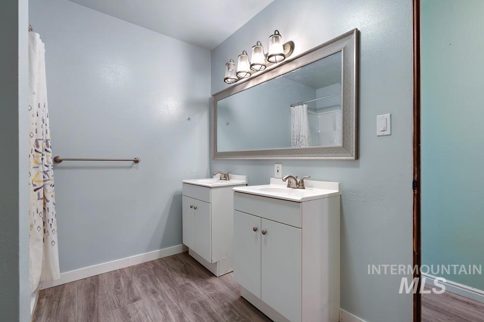 Bathroom with light wood-type flooring, two vanities, and a shower with curtain