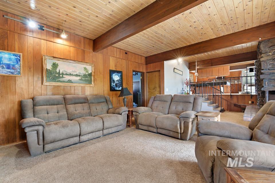 Living room featuring wooden walls, carpet flooring, a wooden ceiling with exposed beams, and a stone fireplace