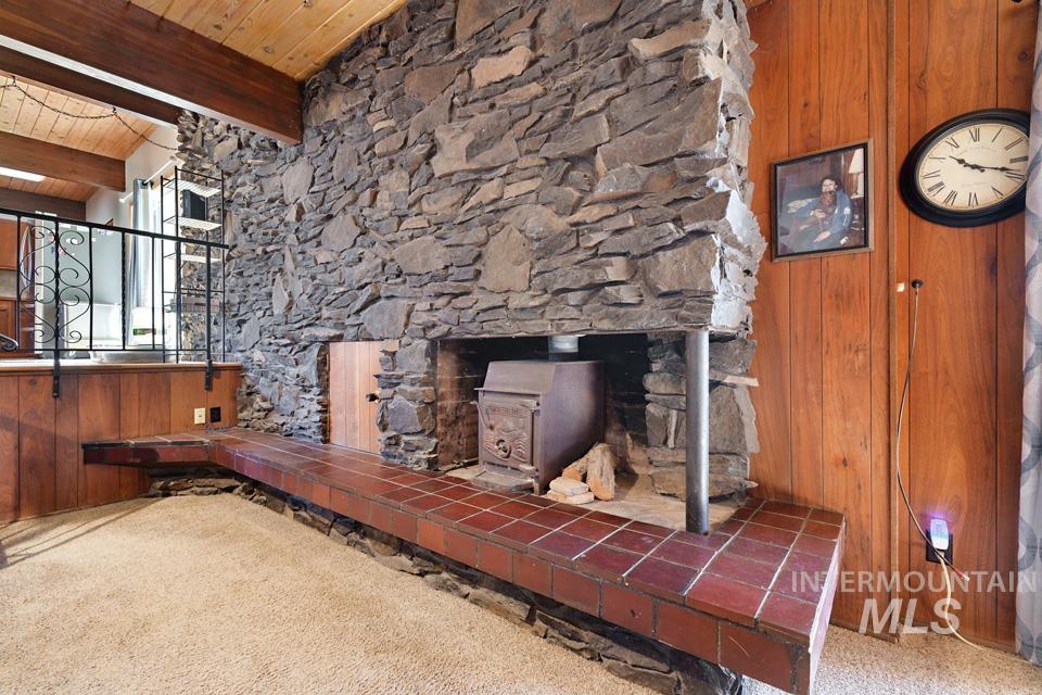 Detailed view of a wooden ceiling with exposed beams, a wood stove, carpet floors, and wood walls