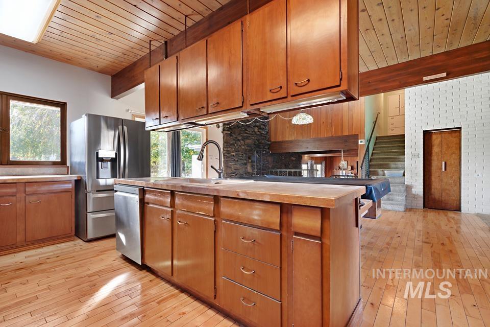 Kitchen with a wooden ceiling with exposed beams, light wood-style flooring, appliances with stainless steel finishes, brown cabinets, and light countertops