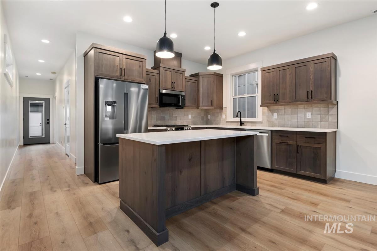 Kitchen featuring appliances with stainless steel finishes, pendant lighting, decorative backsplash, a center island, and recessed lighting