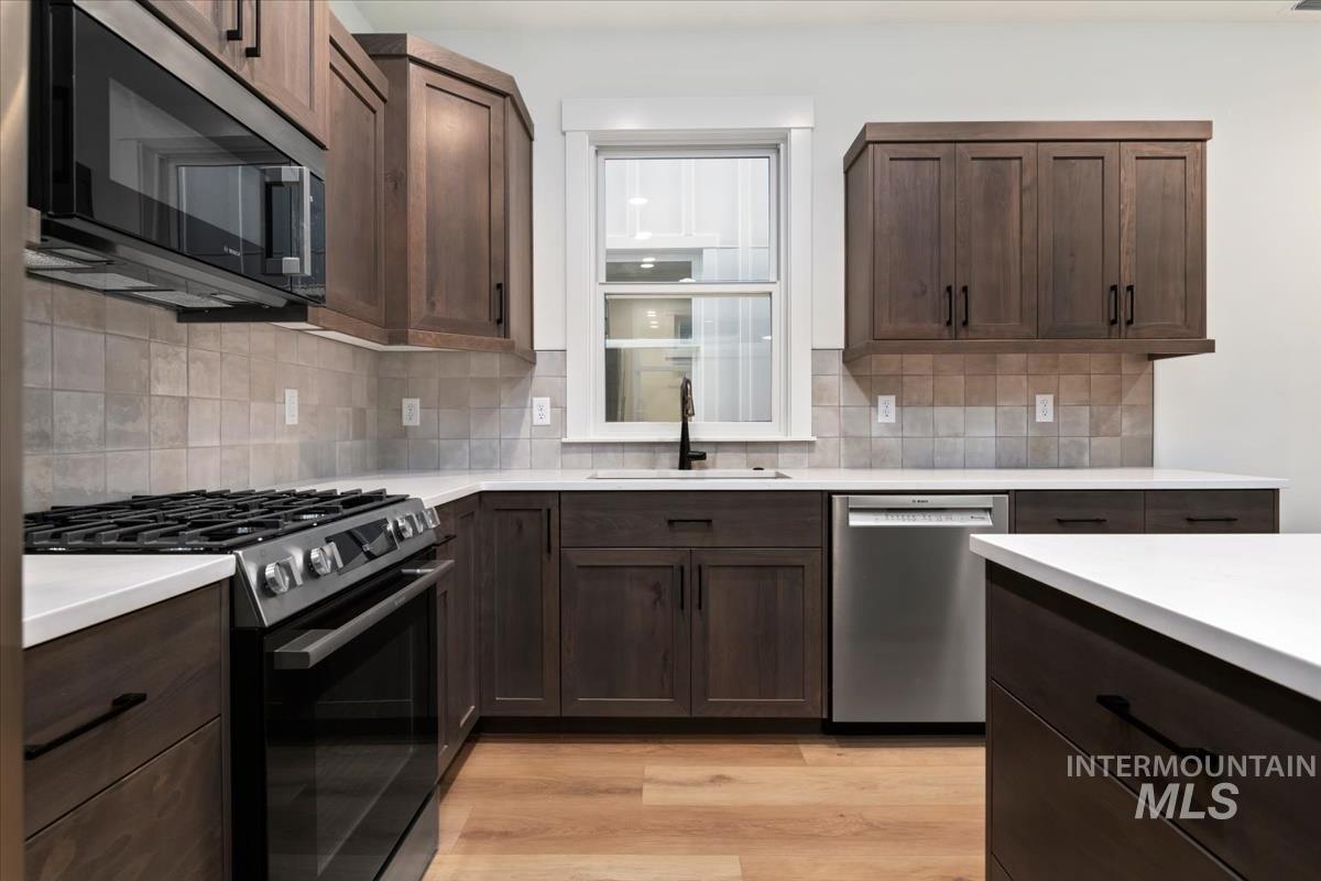 Kitchen featuring gas stove, dishwasher, dark brown cabinets, light wood-style flooring, and backsplash