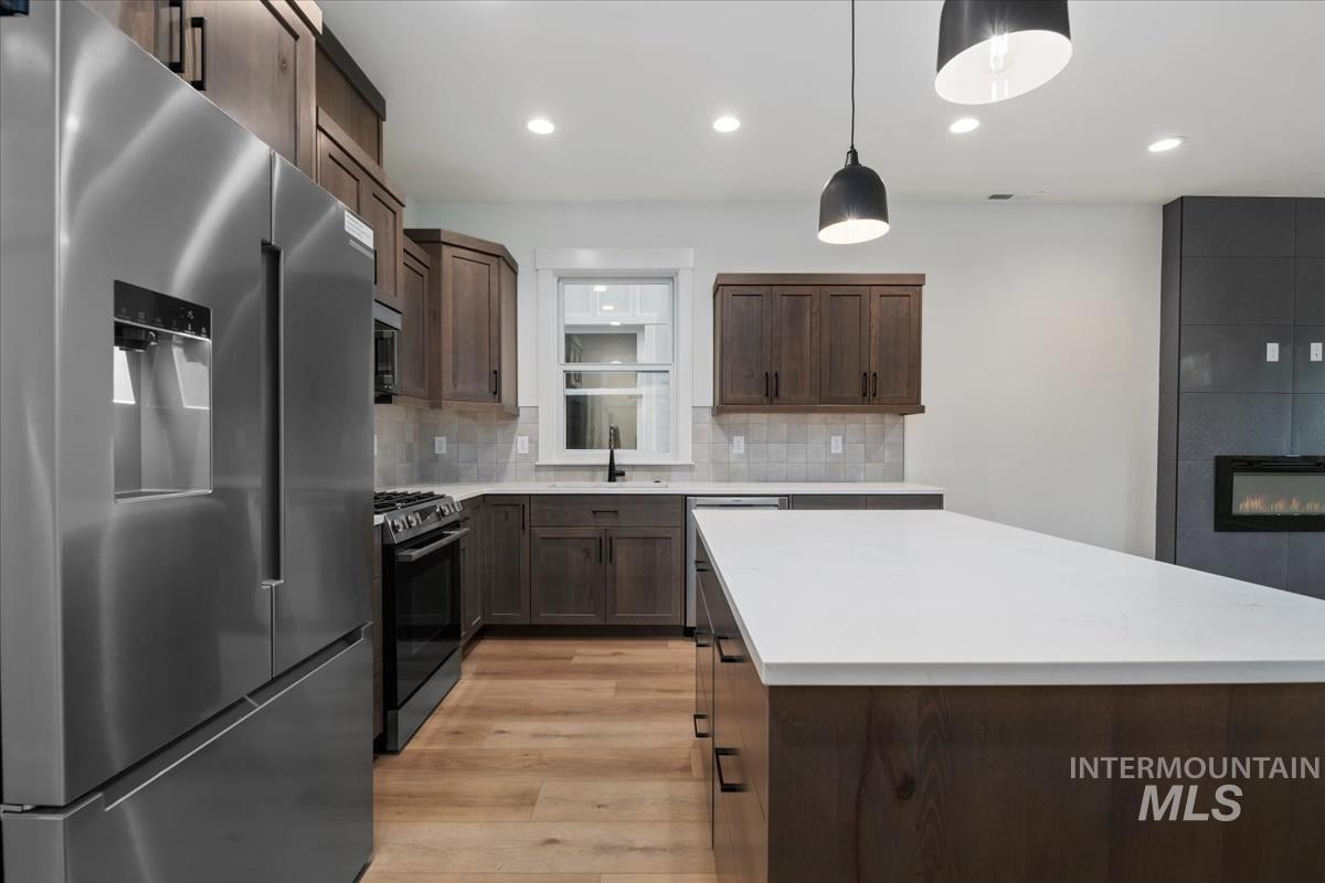 Kitchen with appliances with stainless steel finishes, decorative backsplash, pendant lighting, light wood finished floors, and a center island