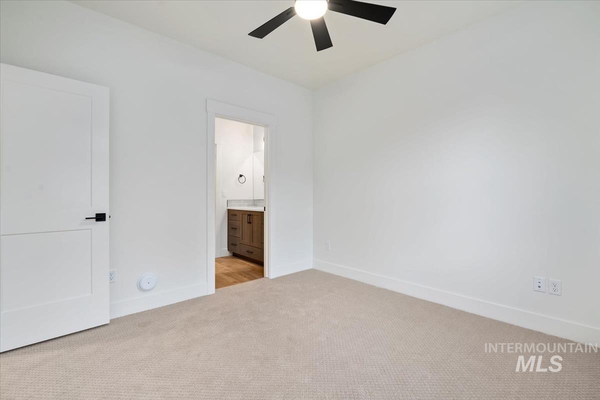 Unfurnished bedroom featuring light colored carpet, connected bathroom, and a ceiling fan